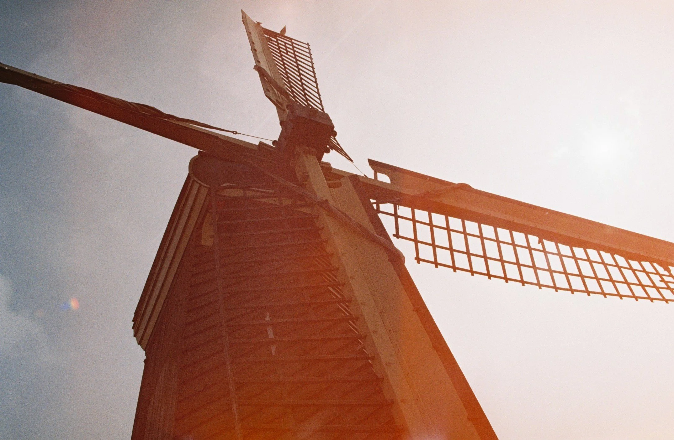 A close-up view of a traditional windmill from below, with the sky in the background and the sunlight creating lens flare.