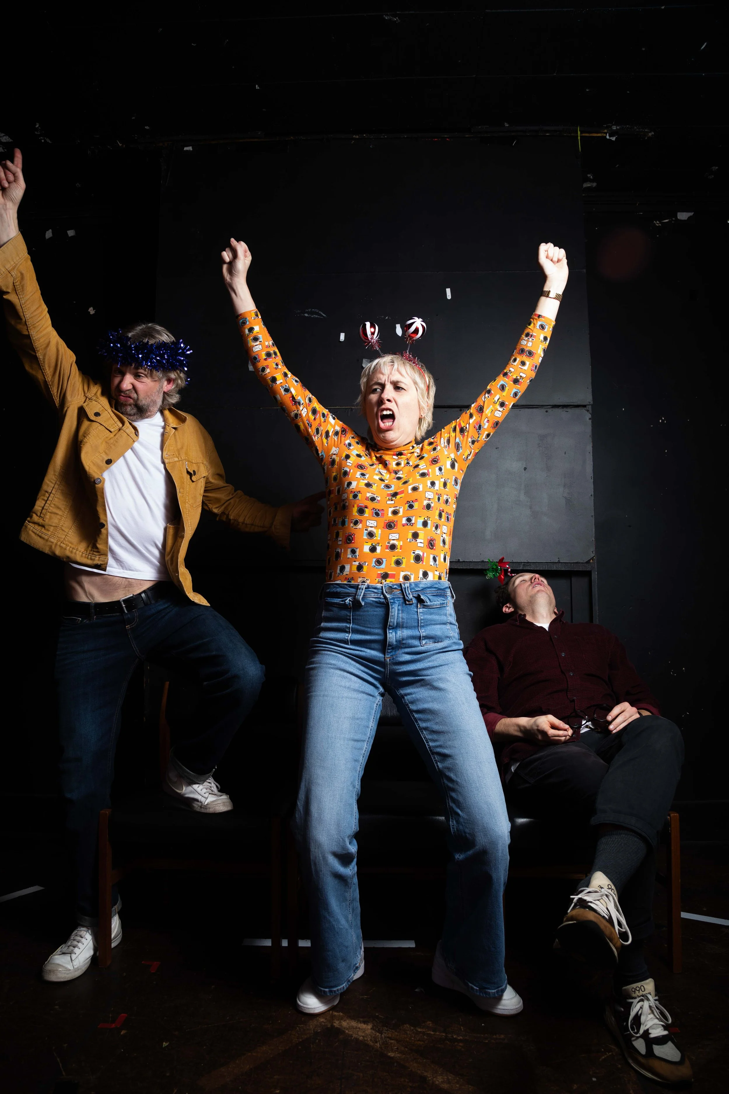 A female comedian wearing a mustard top with a camera pattern called Maisie Adam comedian photographed backstage in a black room by Karina Lax at The Comedy Village, Sheffield