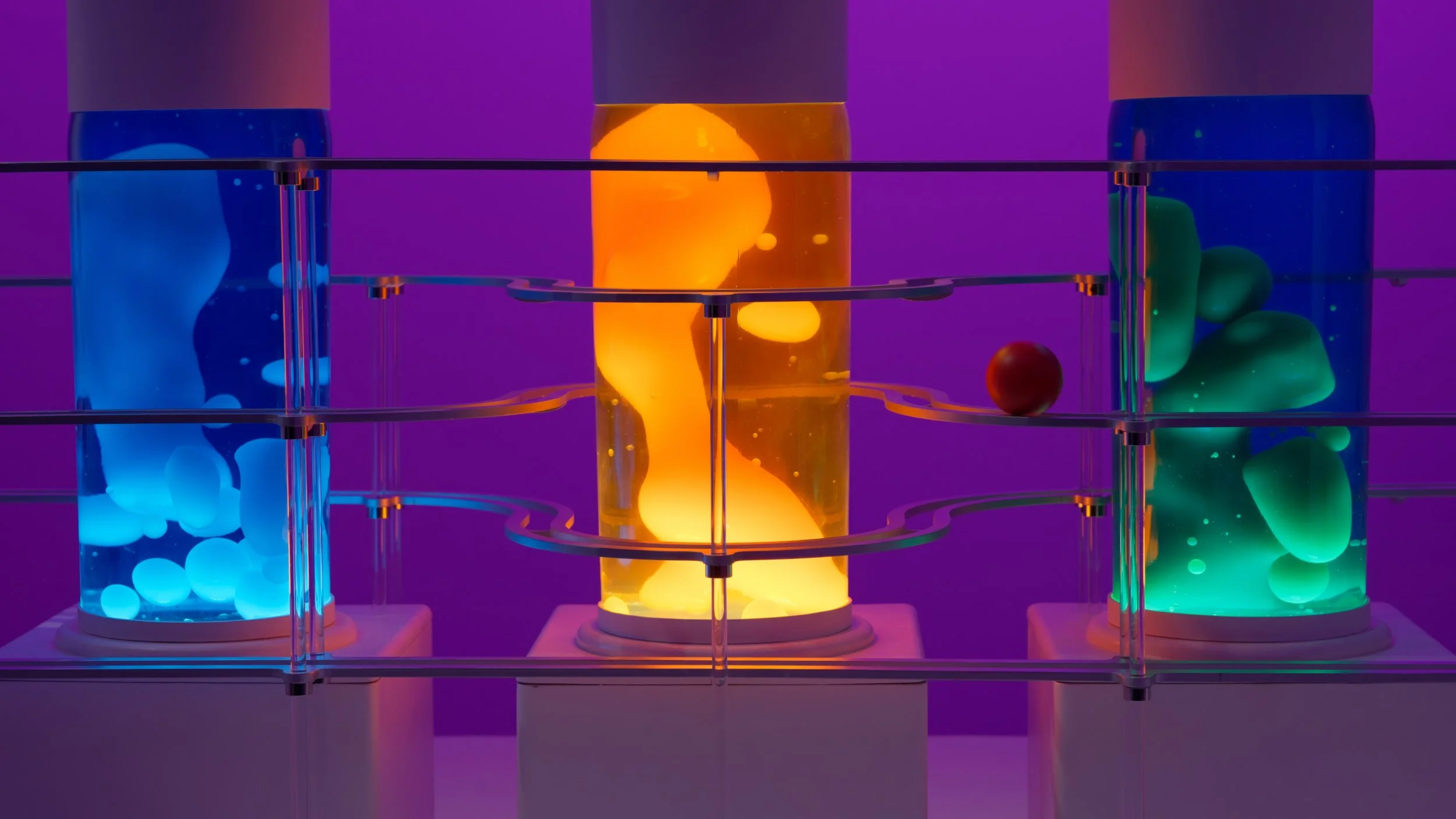 Three glass containers filled with colorful liquids and floating spheres, illuminated with vibrant neon purple, blue, and orange lights.