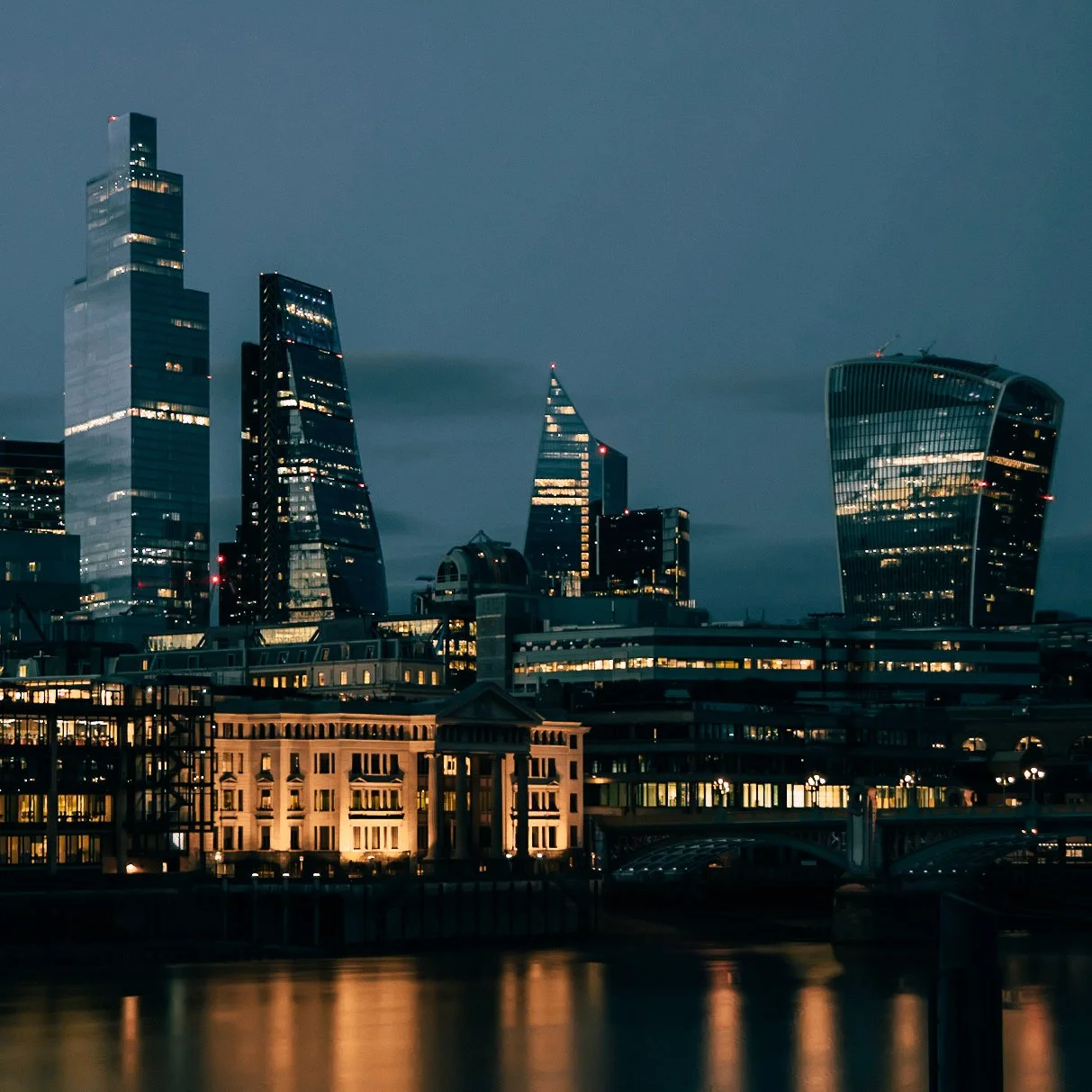 Nighttime cityscape of London featuring modern skyscrapers reflected in the River Thames.