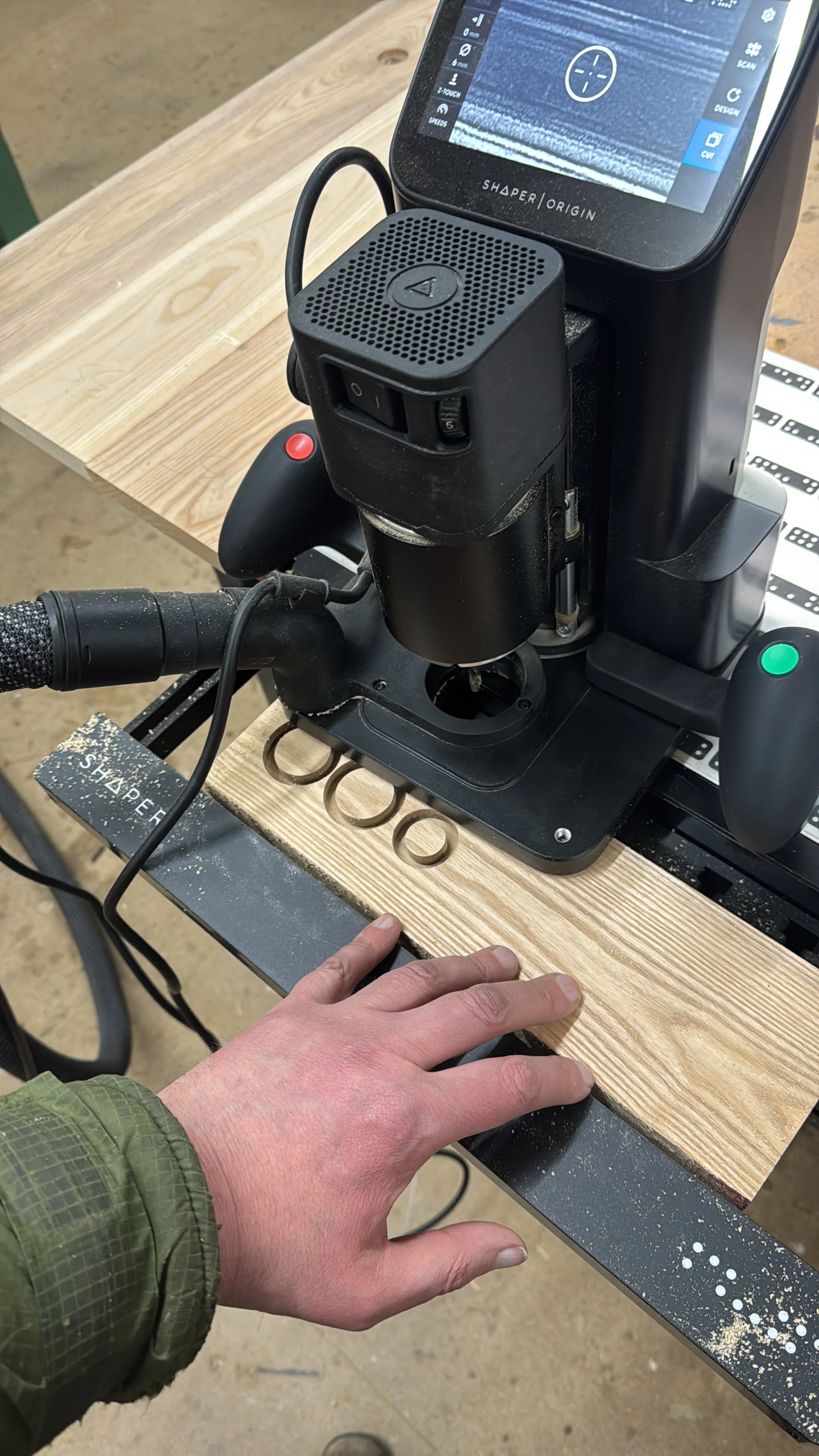 Person operating a CNC machine with a touchscreen control panel, cutting a piece of wood on a workbench.