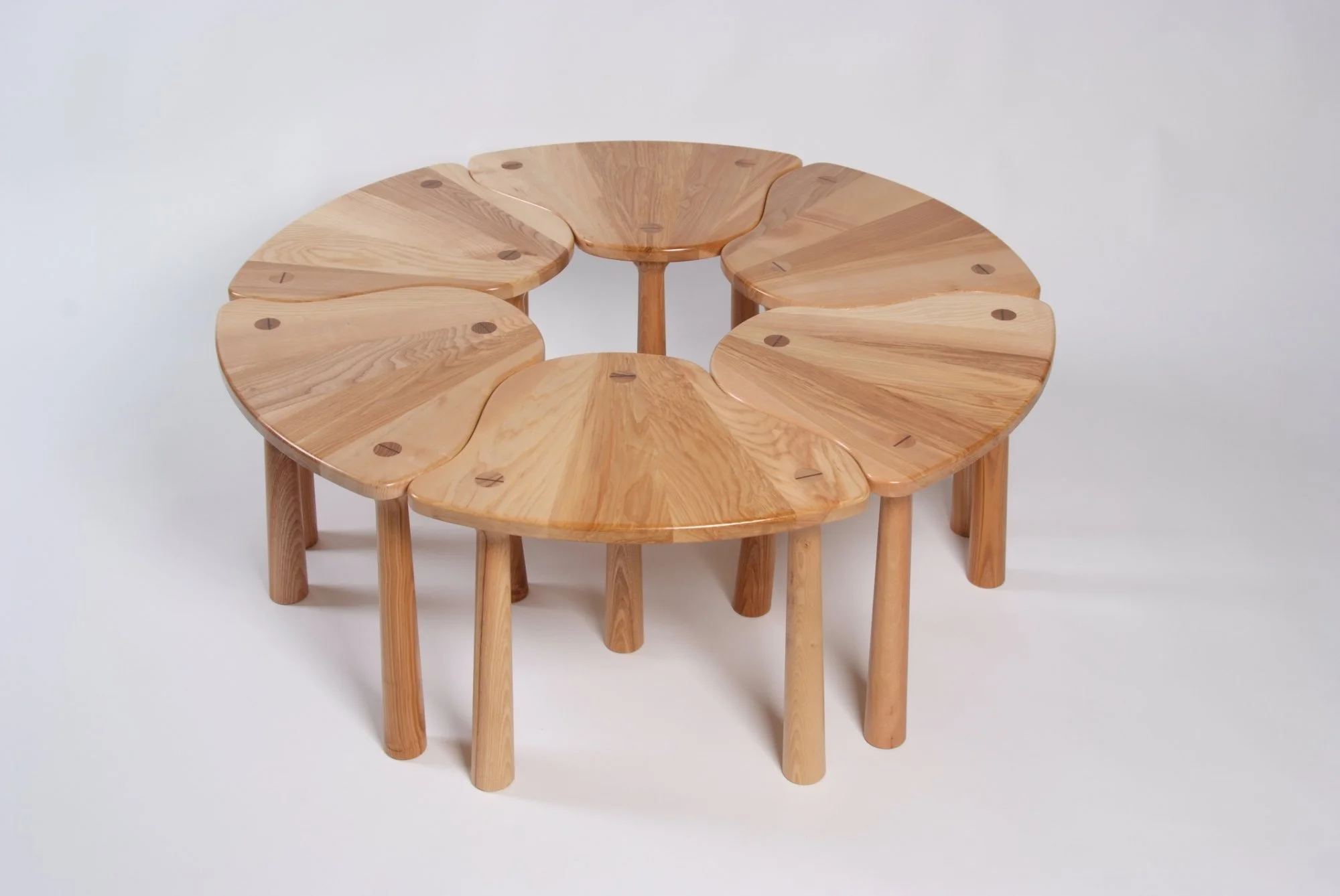 Set of six interconnected wooden stools with rounded seats arranged in a circle against a plain white background.