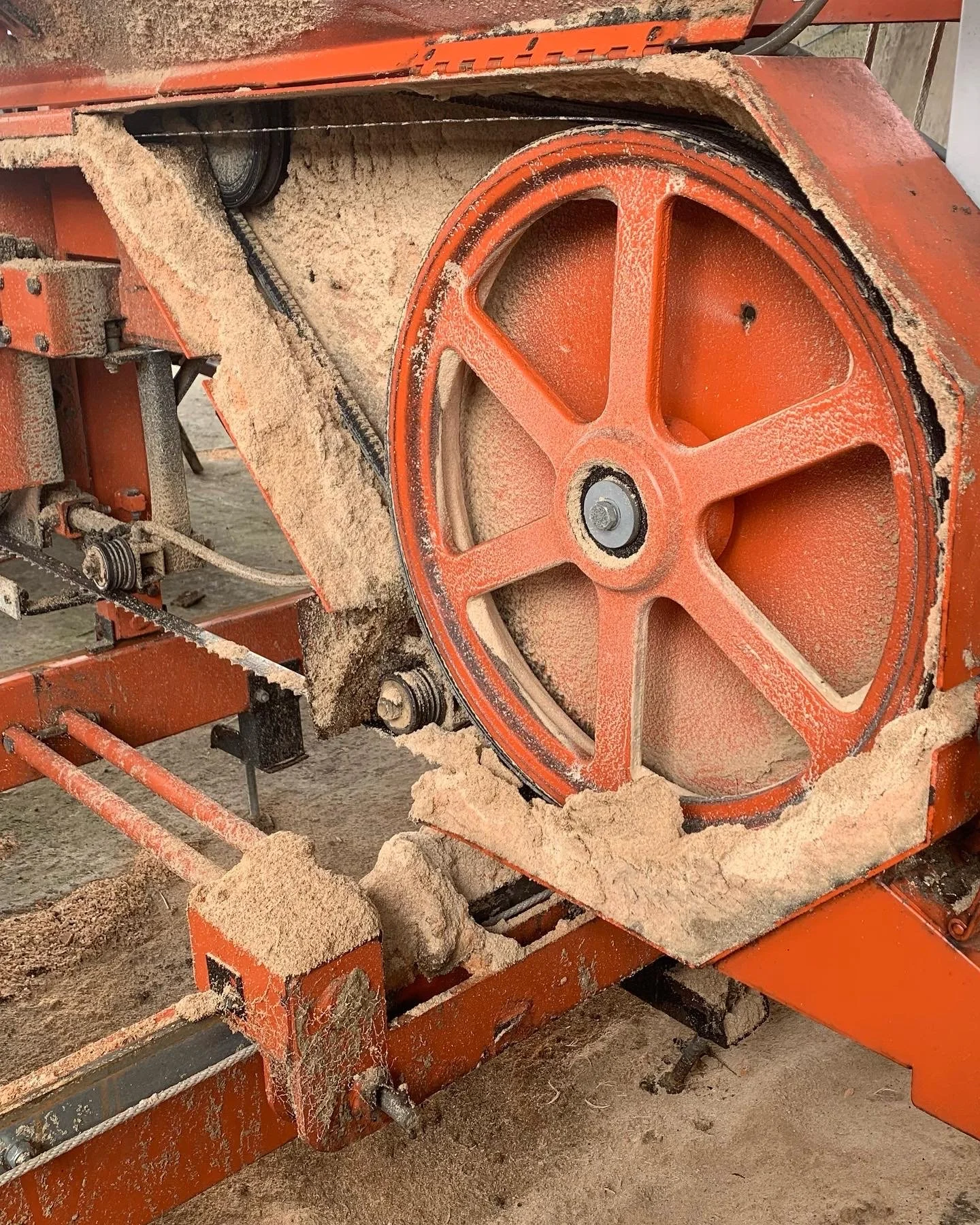 A close-up of an orange concrete saw machine covered in sawdust, with its large circular blade partially visible.