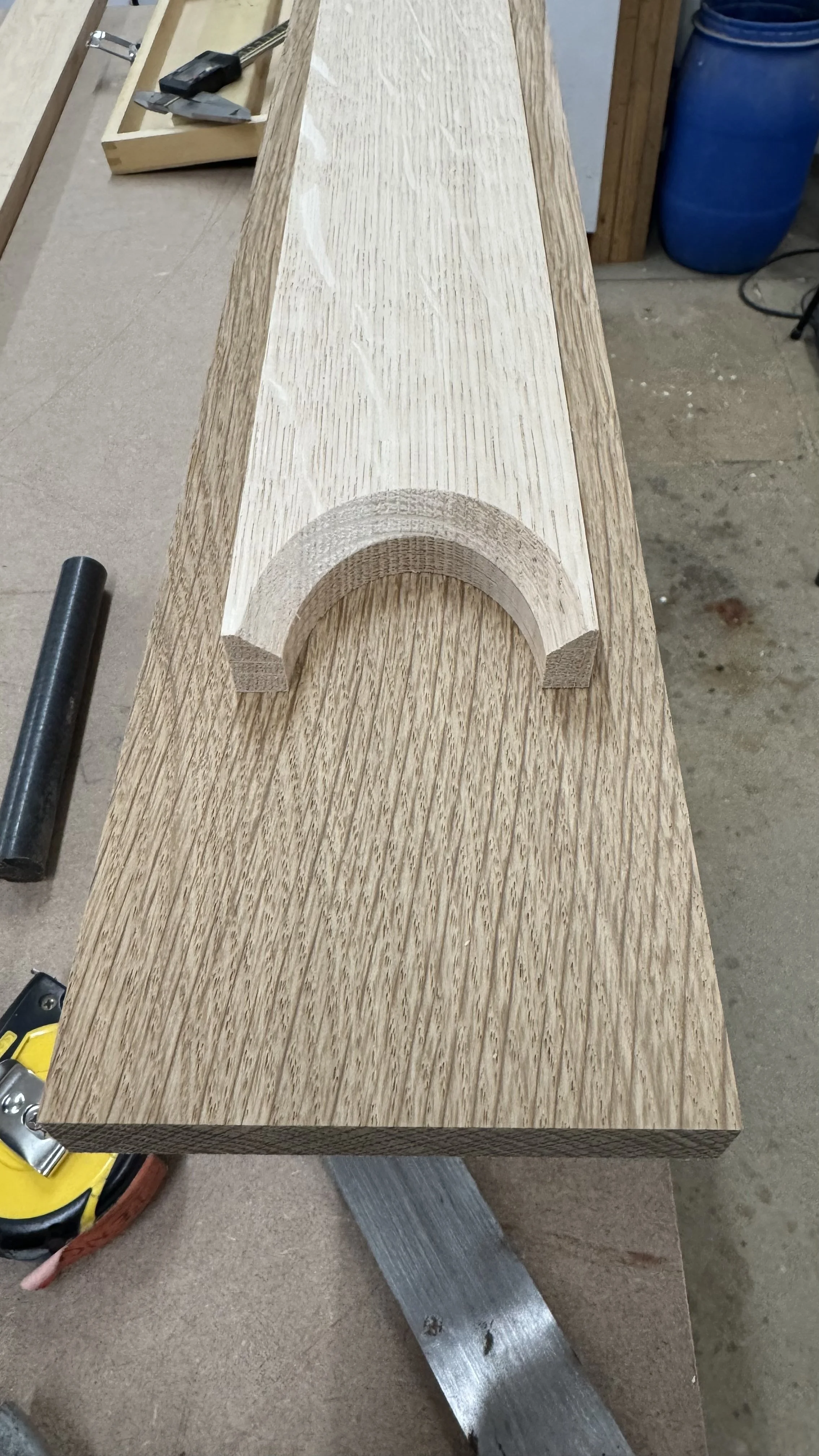 A piece of wood with a semi-circular cutout on top, lying on a workbench in a woodworking workshop.