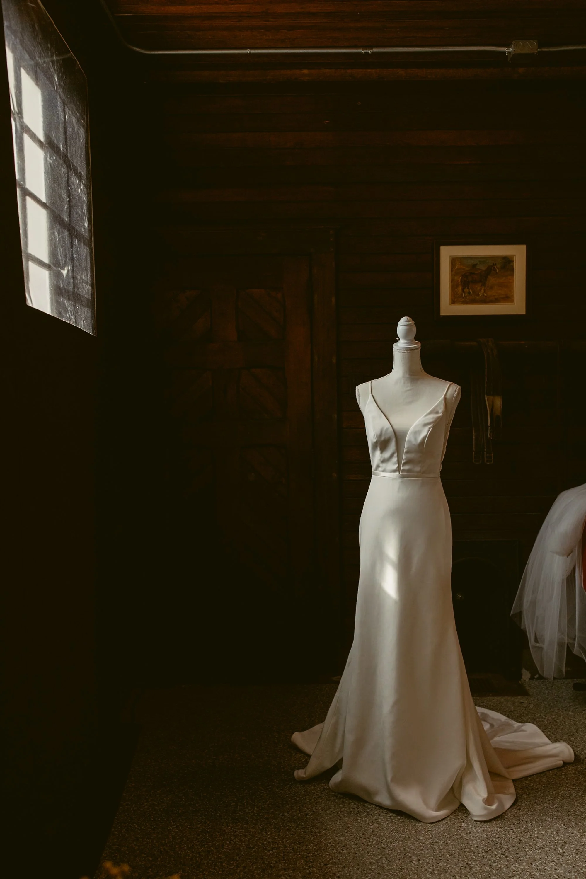 Wedding dress on a mannequin in a dimly lit room with wooden walls.