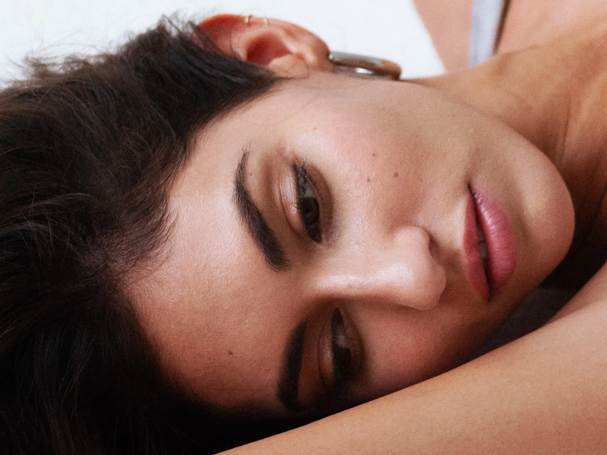 Close-up of a woman lying down with her eyes closed and head resting on her arm.
