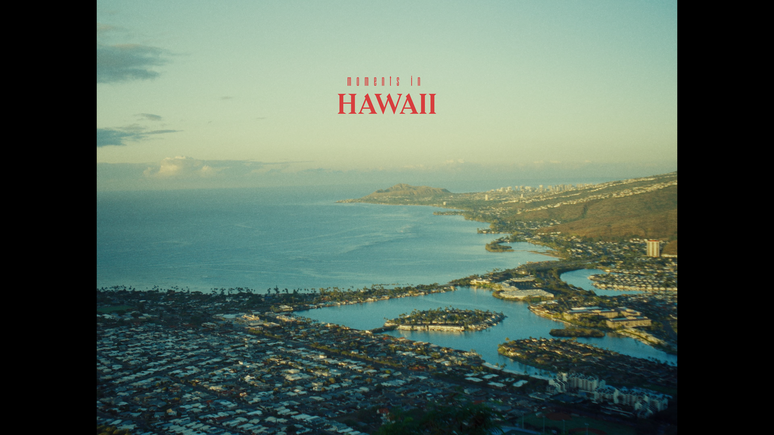 Aerial view of the coastline of Hawaii with ocean, cityscape, and hills during sunset.