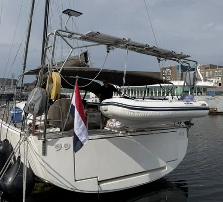 A sailboat docked at a marina with a solar panel mounted above it and gray overcast sky.