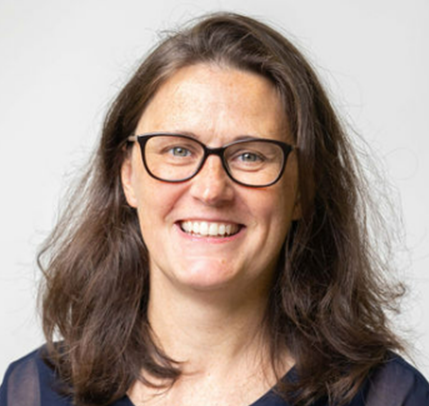 A woman with long brown hair, wearing glasses, smiling, against a neutral background.