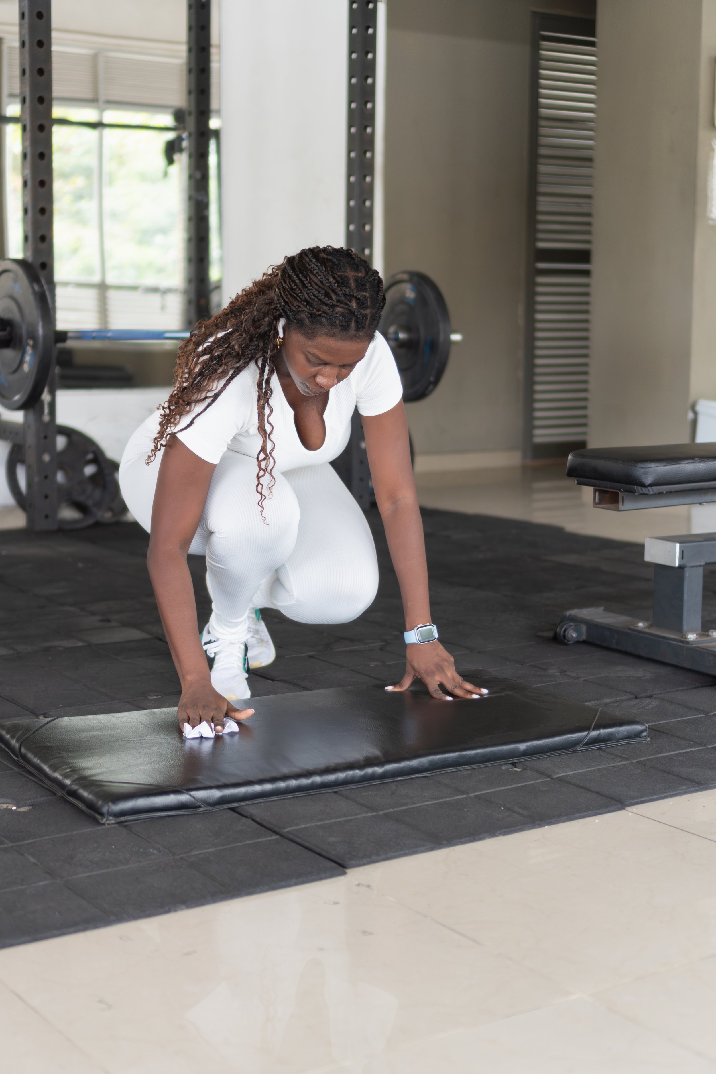 A woman in white athletic clothing is doing push-ups on a padded mat in a gym.