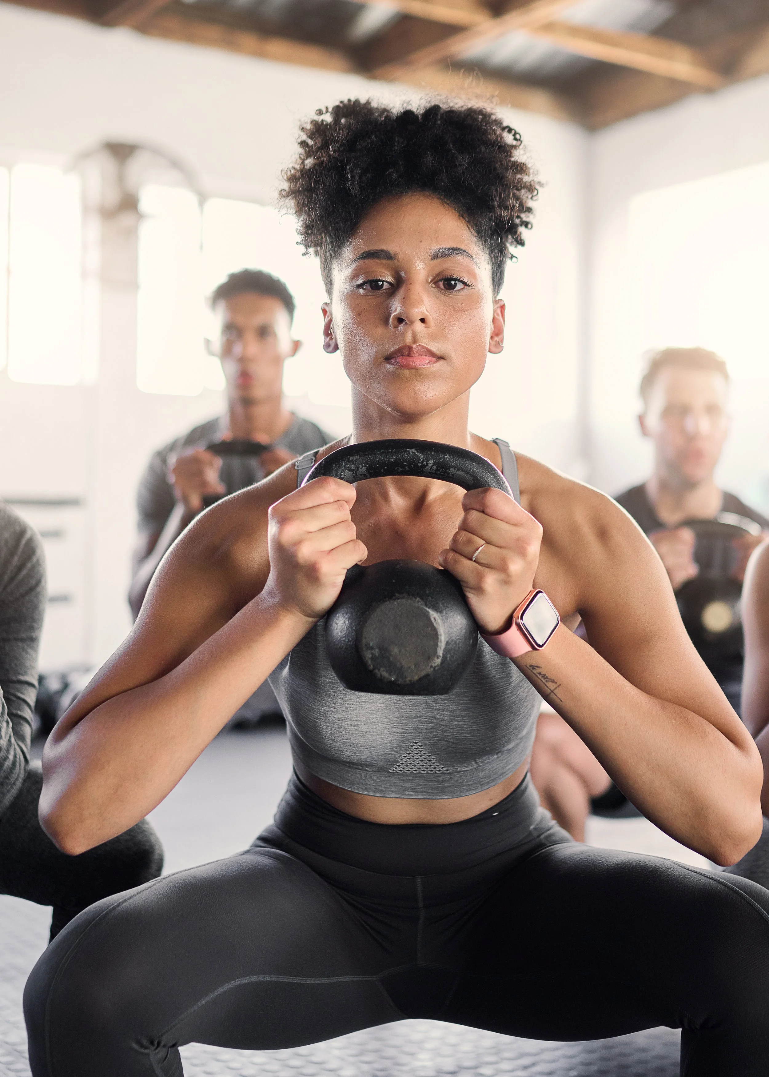 A woman holding a kettlebell during a workout class with other people in the background.