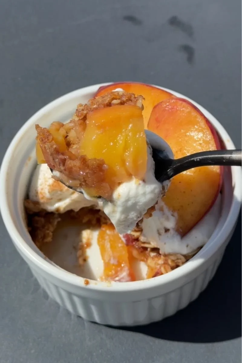 a spoon hovering over a ramekin of peach crisp