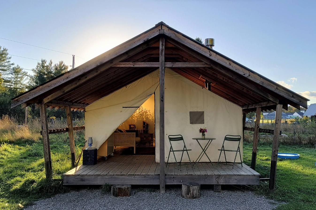 Large wall tent with metal roof, chimney and cafe table on porch.