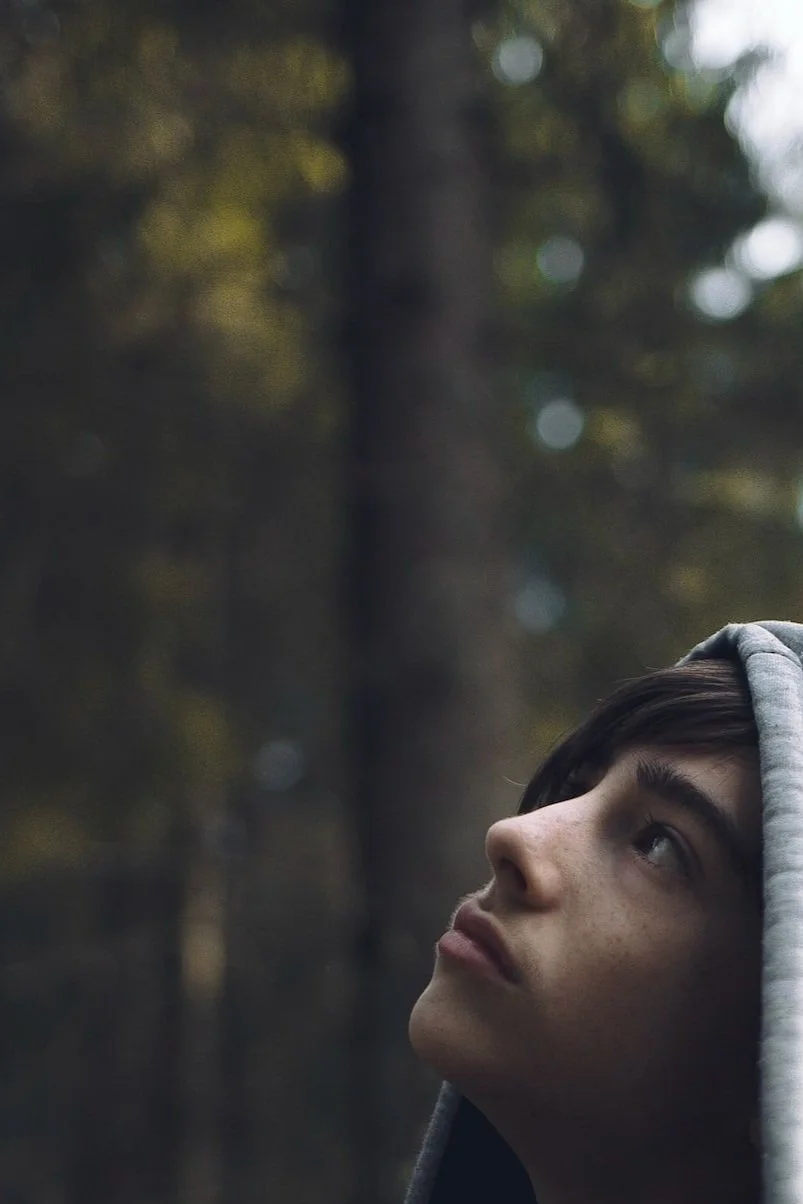 Teenager with gray hoodie gazing up at the trees deep in thought