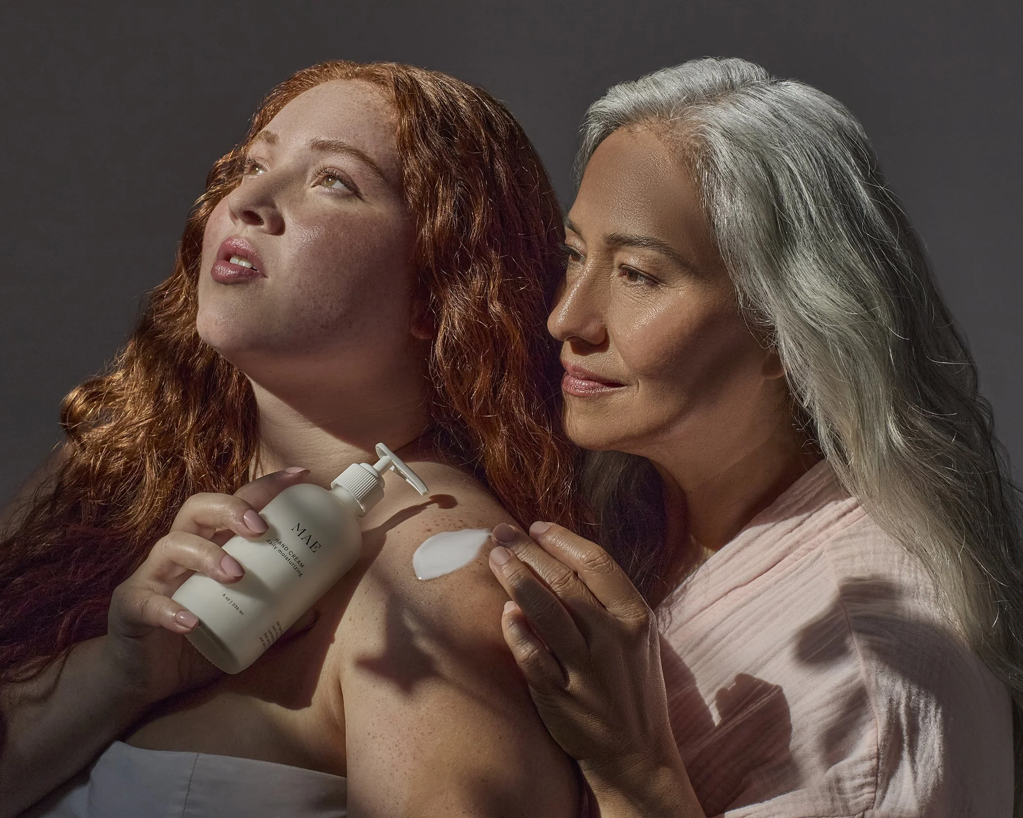 Two beautiful Latinx women, one young 20's the other elder with long grey hair try a lotion in a caring beautiful moment of care. 