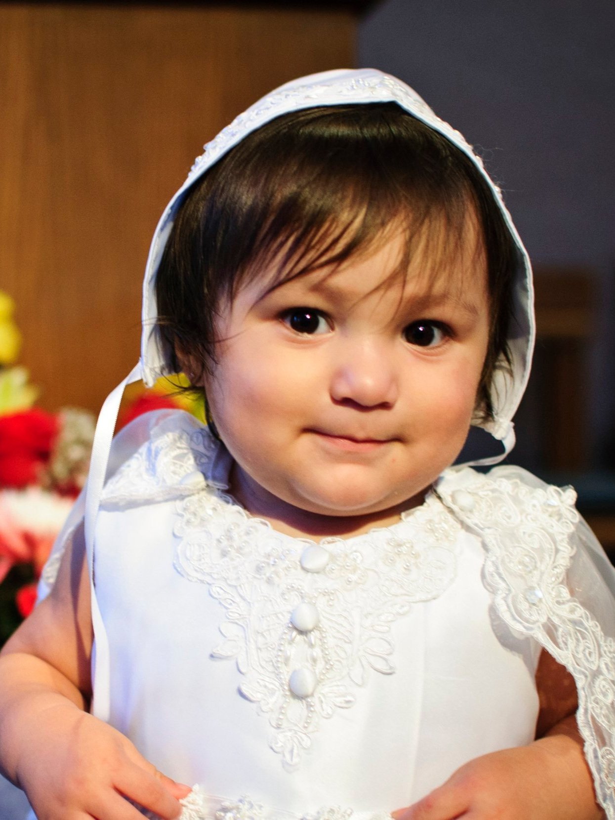 A young child wearing a white, lace-trimmed dress and bonnet.
