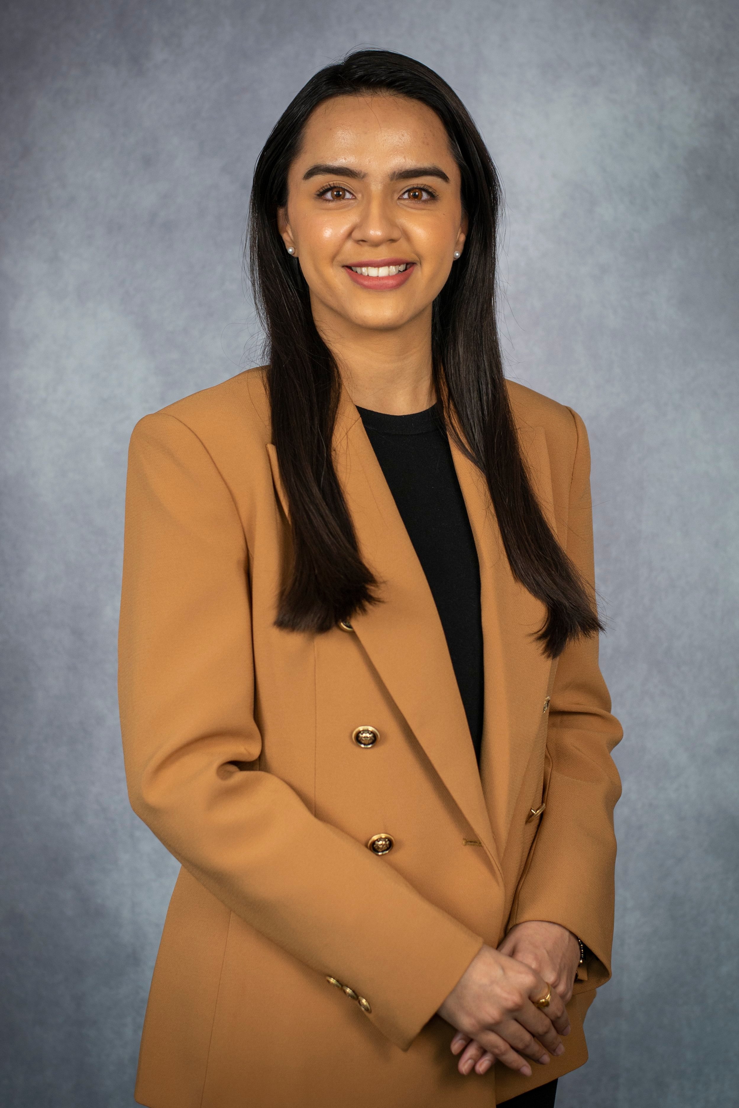 Woman wearing a tan blazer posing against a gray background.