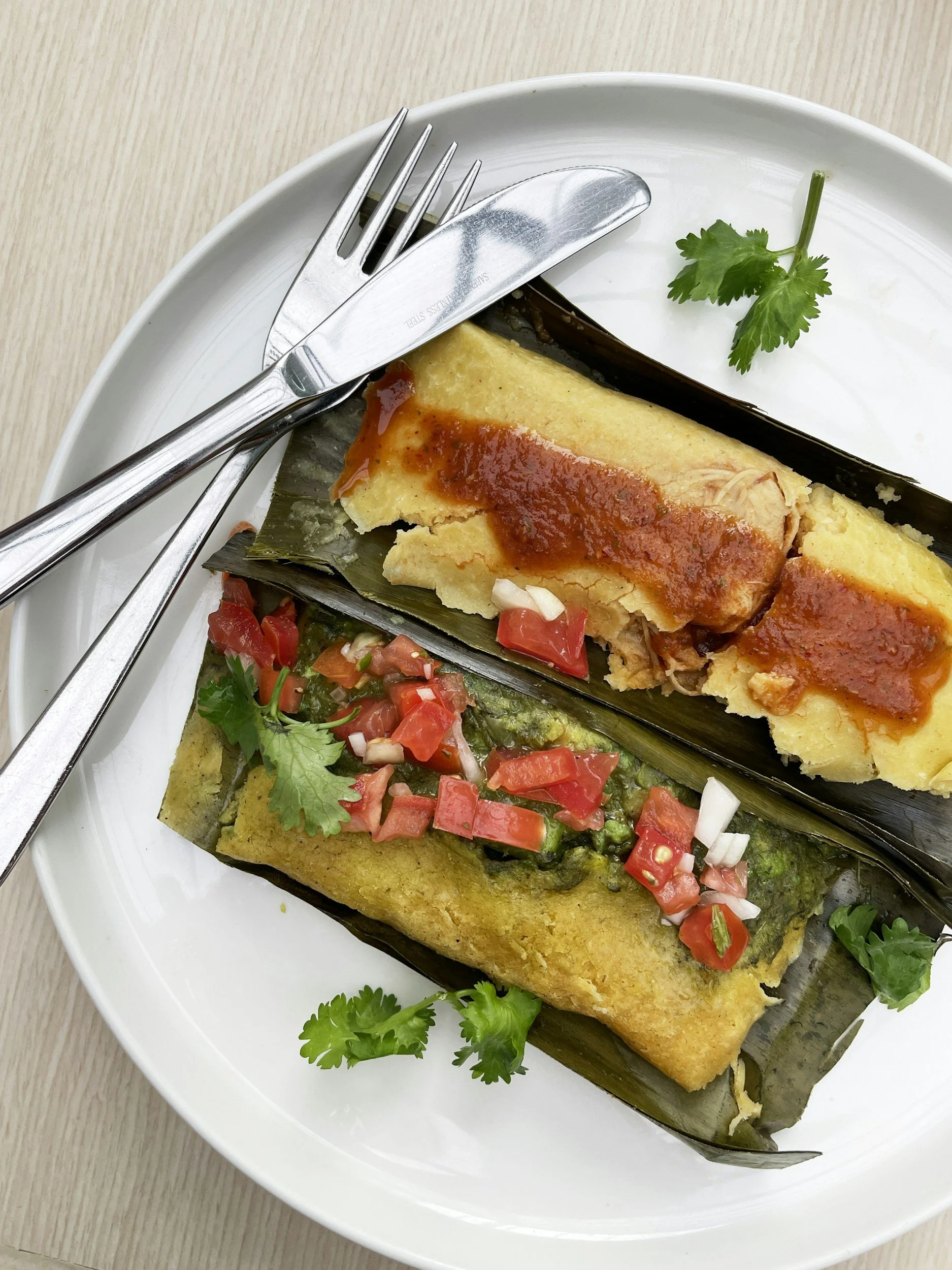 Tamales sitting within leaves on a plate