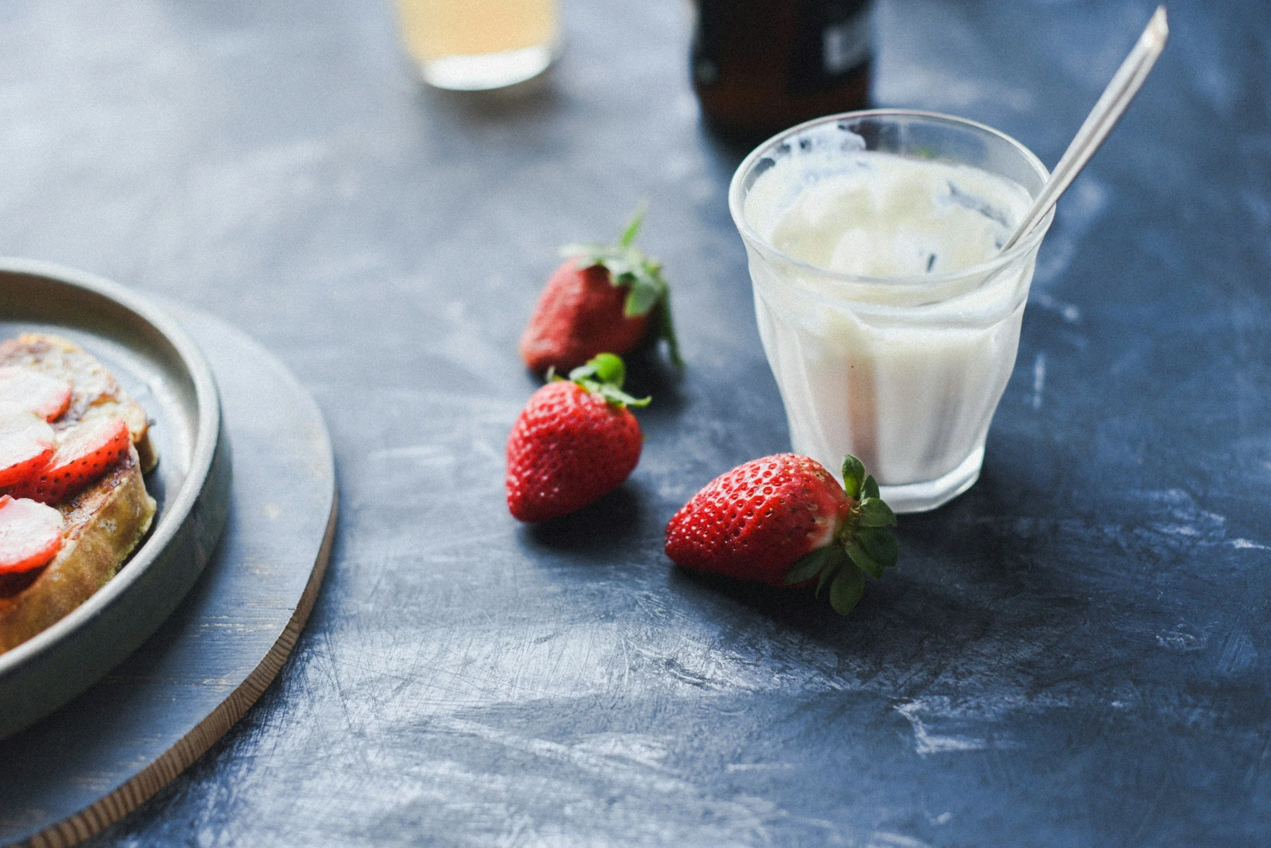 A cup of yogurt on a table with strawberries