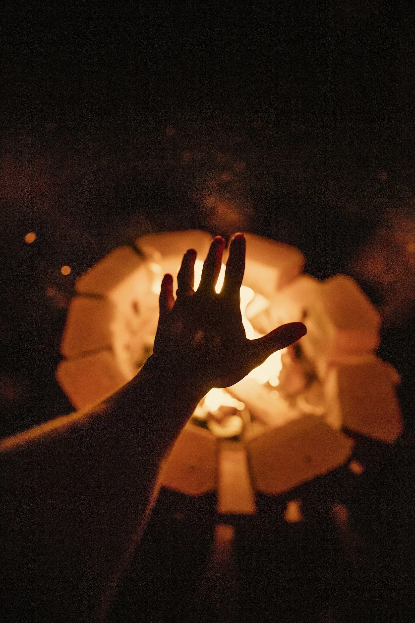 A hand reaching out to feel the heat of a campfire at night