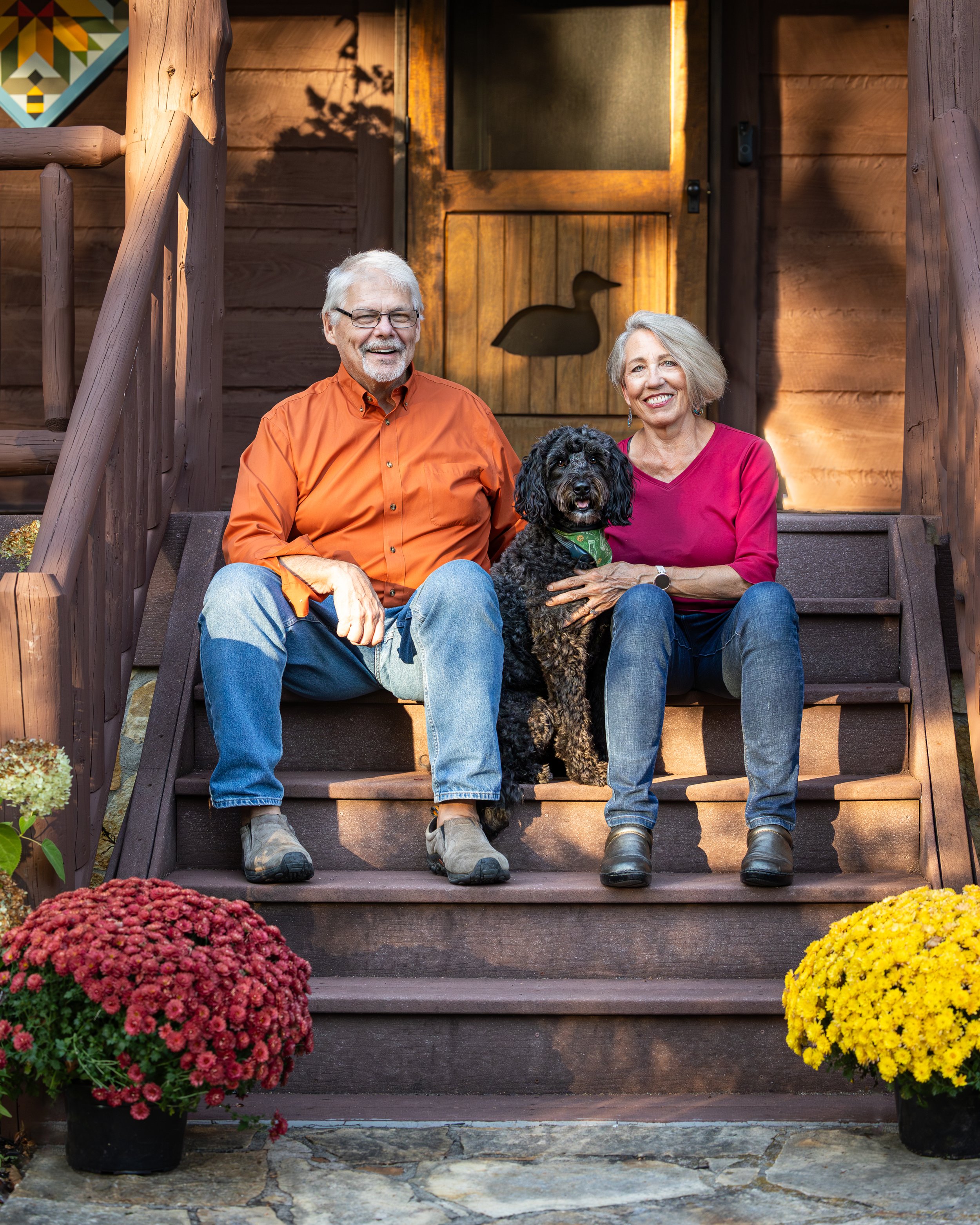 Husband and wife sitting on their porch with their labradoodle sitting in between them.