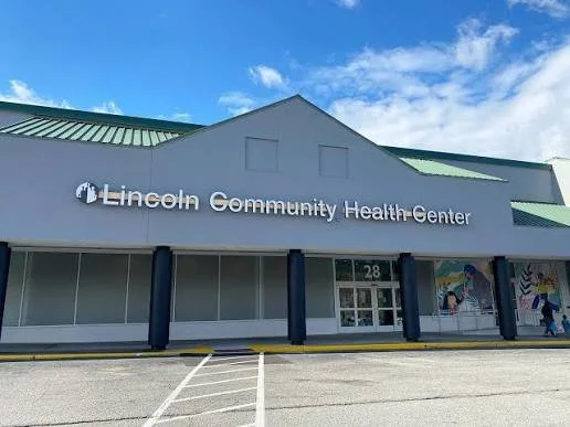 Front view of Lincoln Community Health Center storefront with parking lot and blue sky