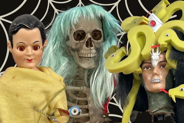 Display of Halloween decorations including a Frida Kahlo-inspired doll, a skeleton with long turquoise hair, and a masked figure with a snake headdress against a black and white web-patterned background.