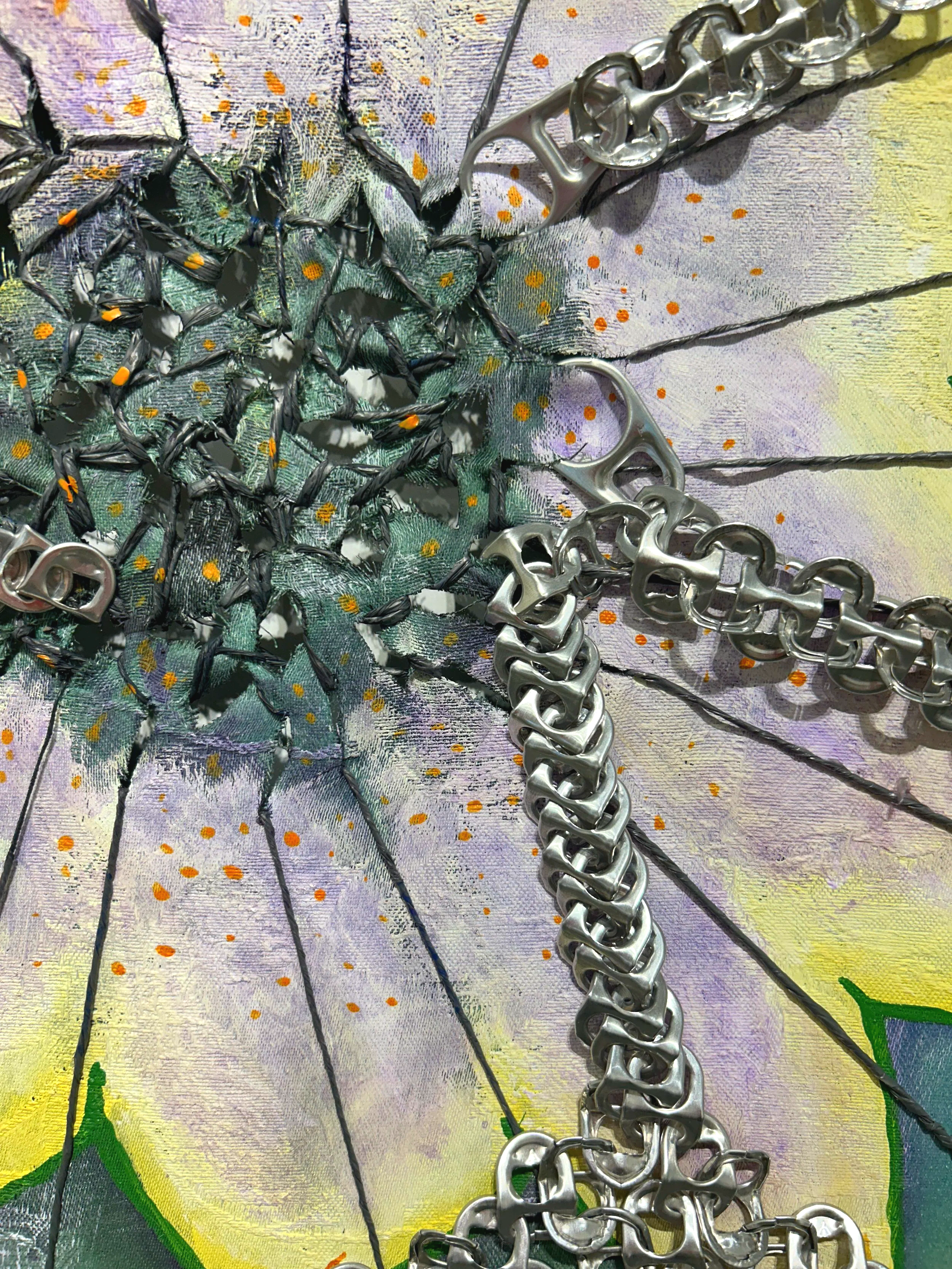 Close-up of a piece of colorful fabric with a printed design, overlaid with various metallic chains and a silver pull-tab, possibly from a soda can, placed on top.