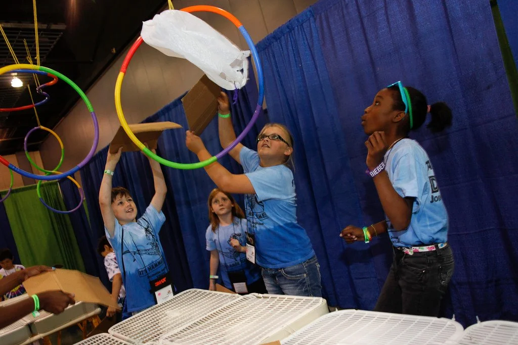 four students doing a challenge, rainbow hoops in the air