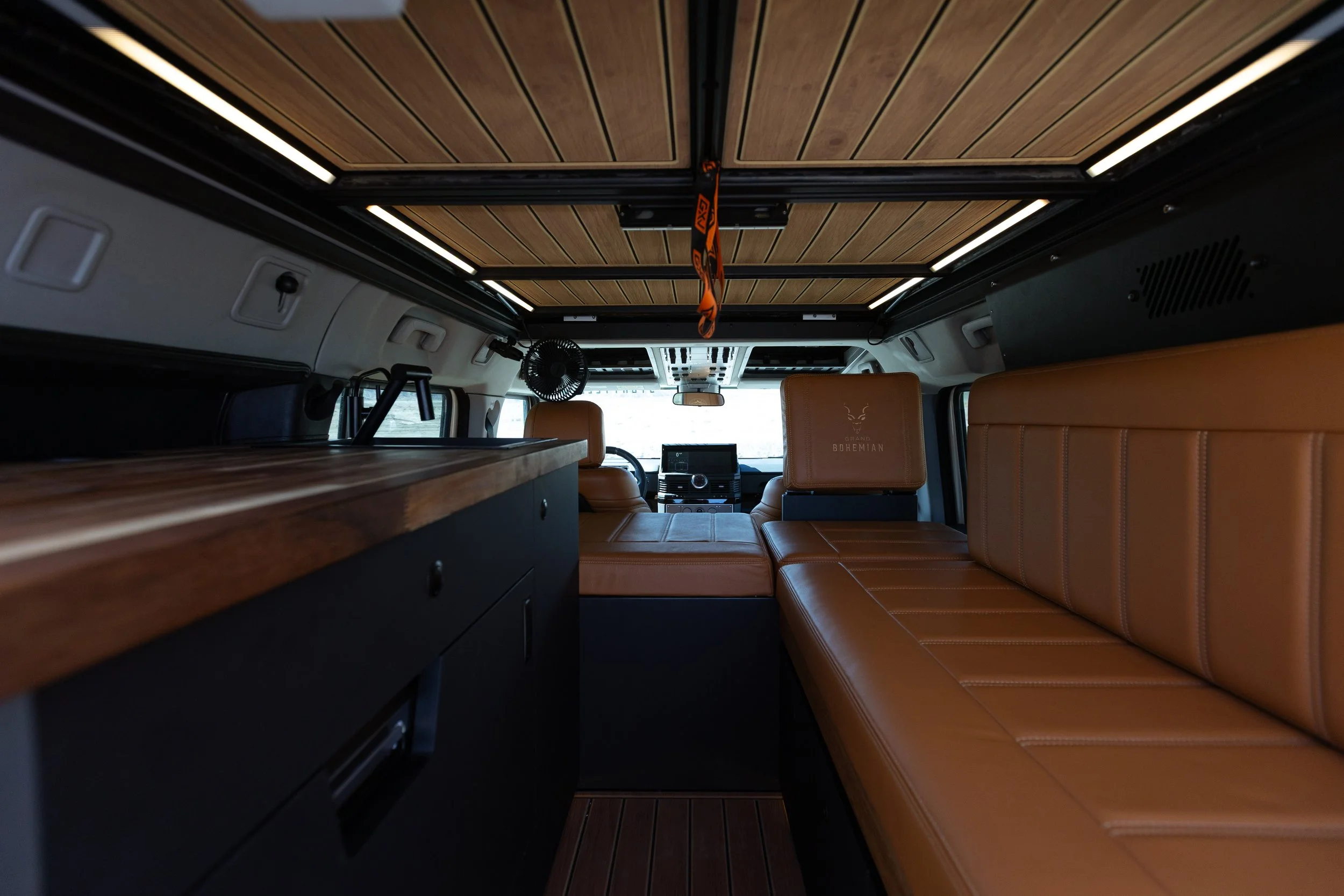 Interior of a customized van with leather seats, wooden ceiling, and a fold-down bed.