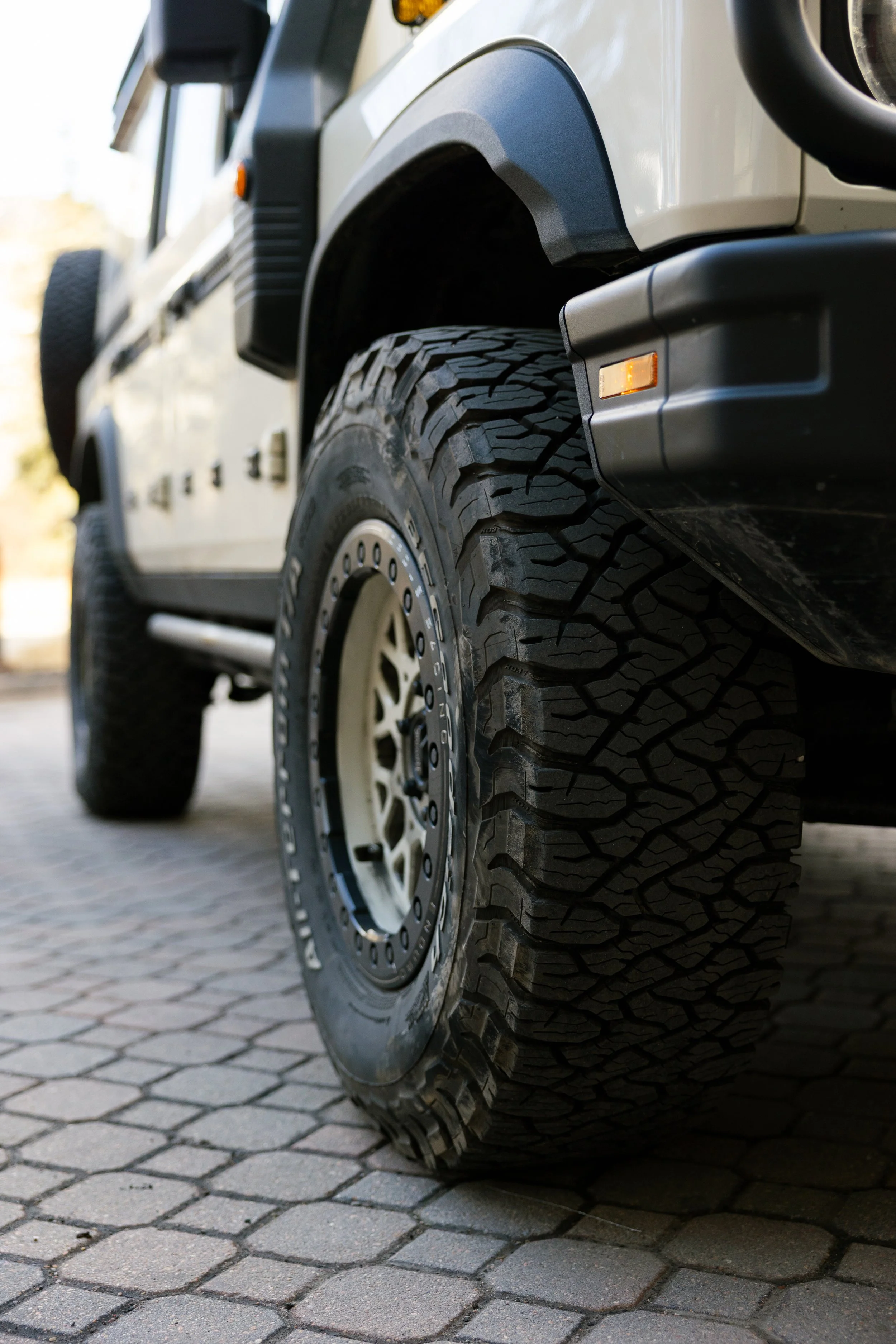Close-up of a rugged off-road tire on a vehicle parked on a cobblestone pavement.
