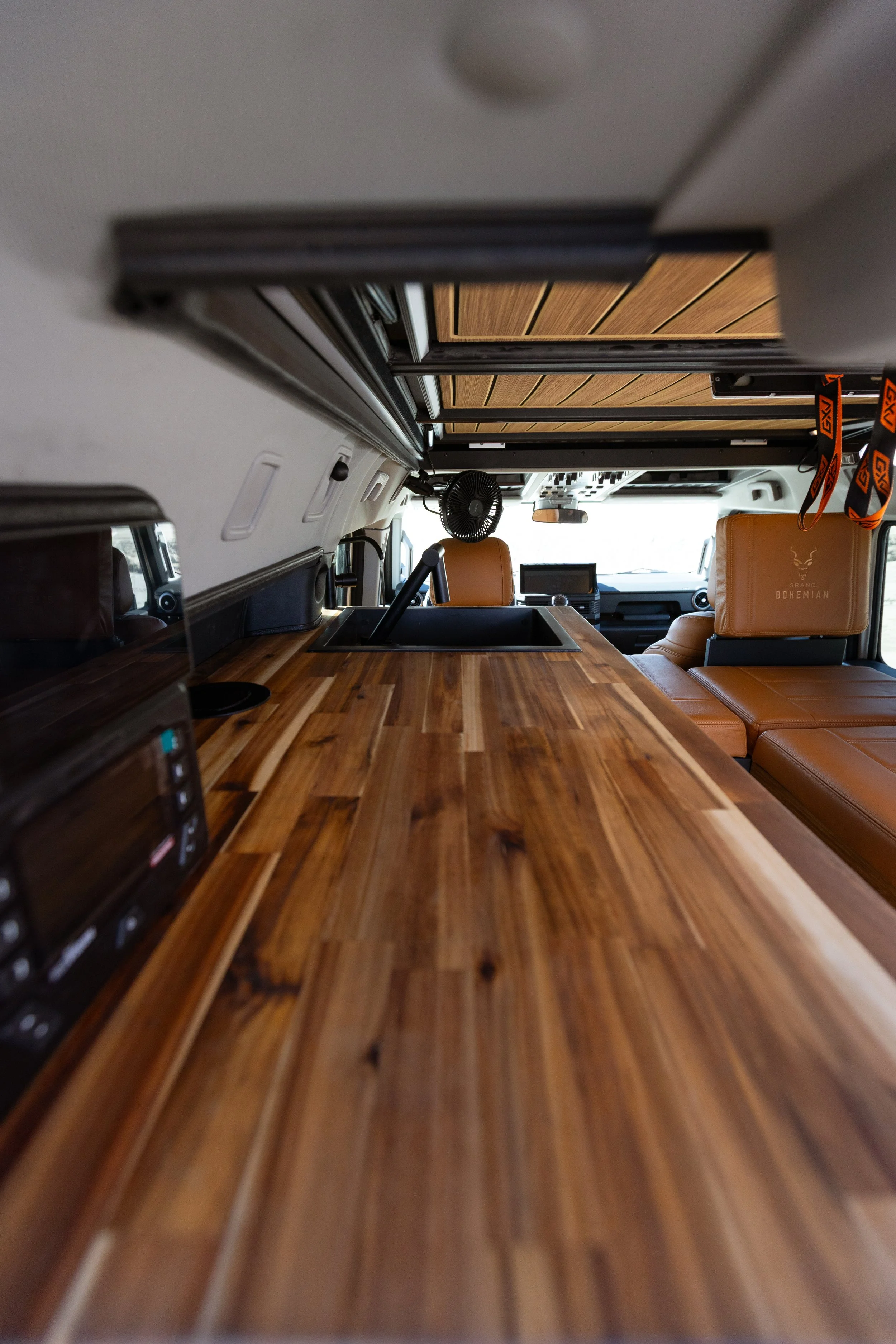 Interior of a camper van with a wooden countertop, a sink, and a seating area with tan leather cushions.