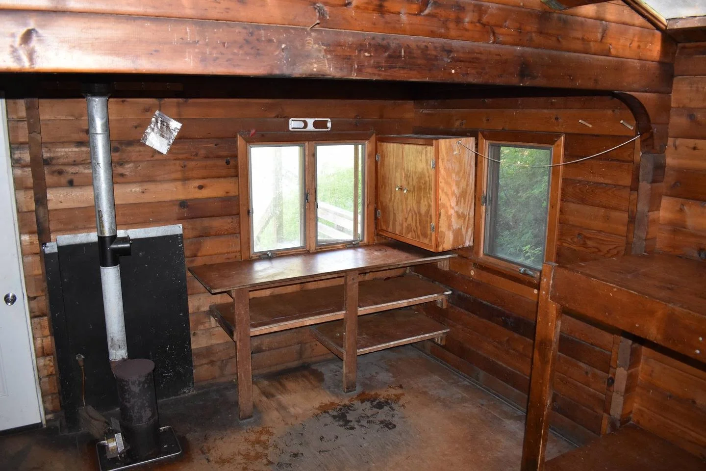 Wooden interior with small window, makeshift workbench, and a wood stove pipe.