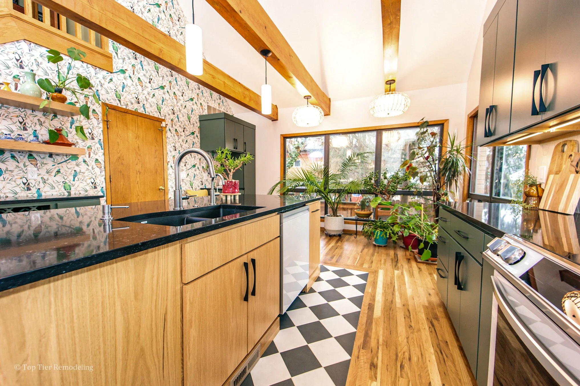 A modern kitchen with wooden cabinets, a black countertop, hanging pendant lights, and large windows. There are numerous potted plants on the countertops and windowsills. The backsplash features patterned wallpaper with birds. The floor has a black a
