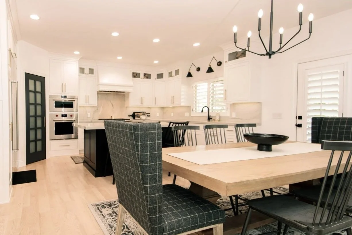 Modern open-concept kitchen and dining area with white cabinetry, a large wooden dining table, black and gray chairs, and black light fixtures.