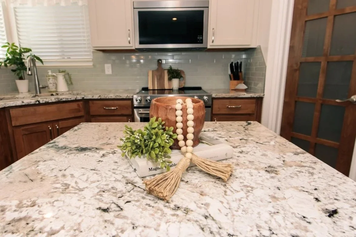 Kitchen countertop with a wooden bowl containing a beaded garland, a small plant, and books on a granite surface.