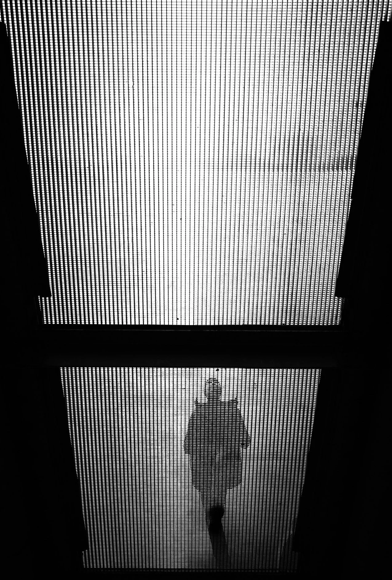 Person walking on an illuminated grid walkway, viewed from below in black and white.