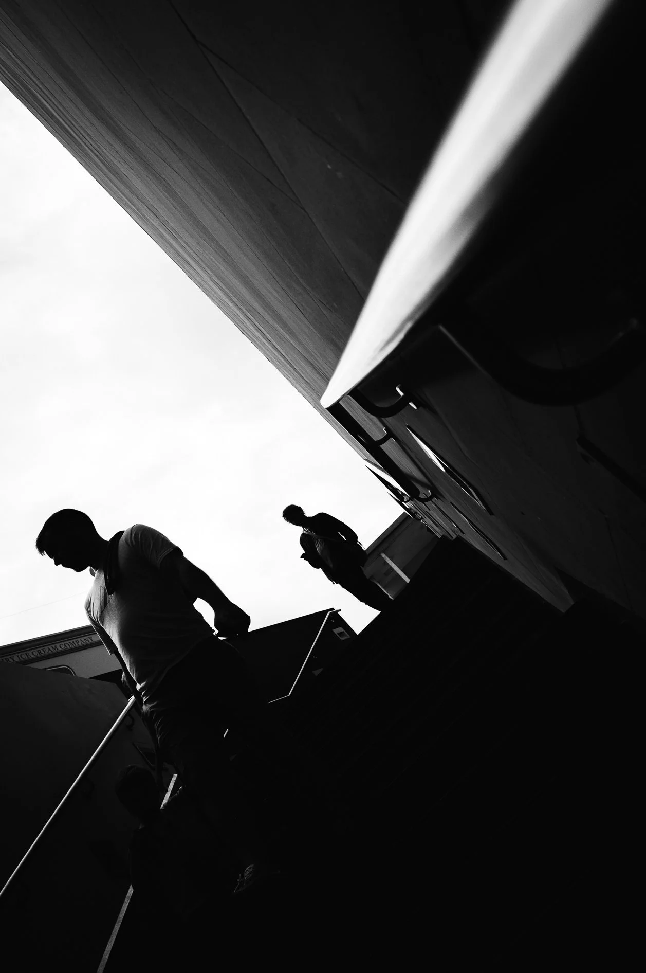 Black and white photo of two silhouetted people on a rooftop, with a large building behind them and the sky above.