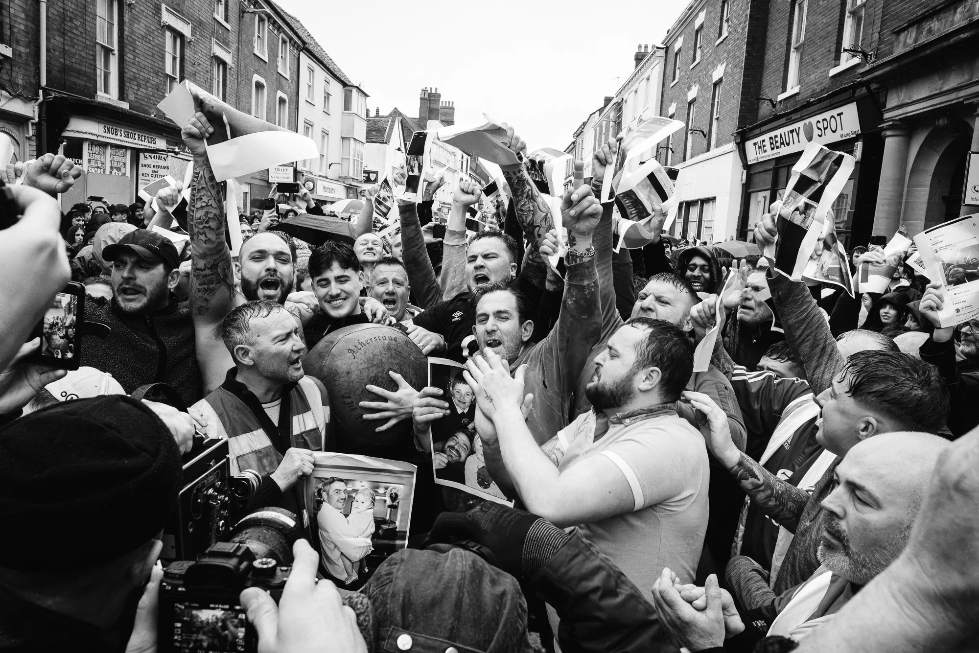 A crowd of people protesting on a street, holding photos and banners, with some embracing and cheering. It appears to be a demonstration or rally.