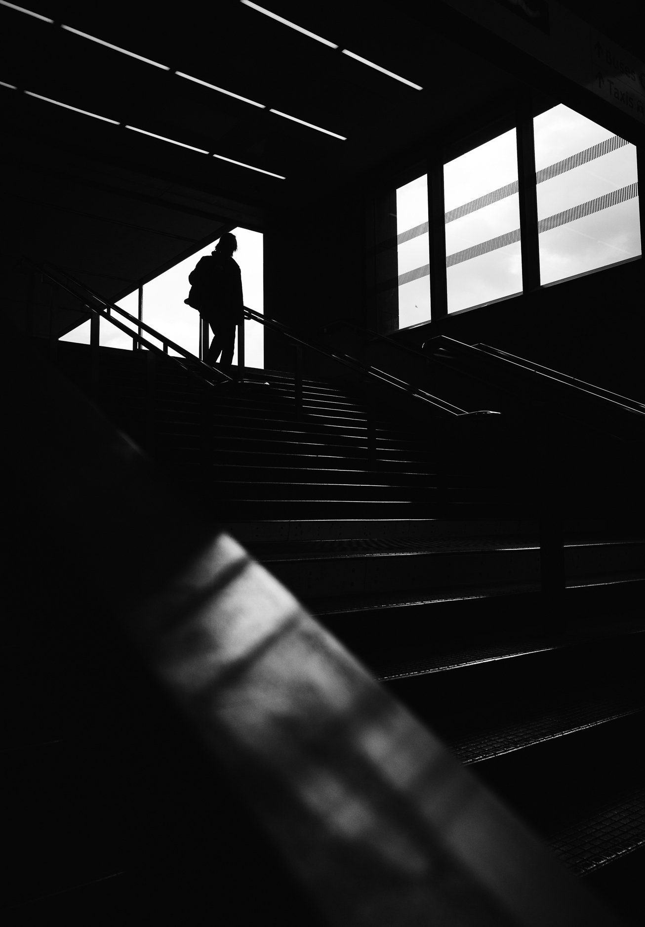 Silhouetted person walking up a staircase inside a building with large windows letting in natural light.