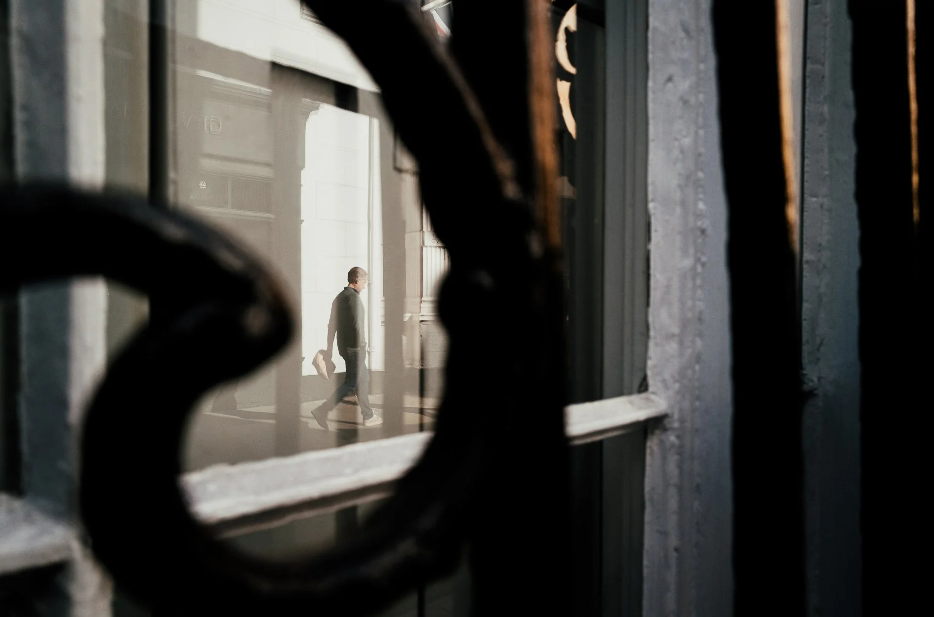 A person walking with a briefcase as seen through a window with black wrought iron bars.