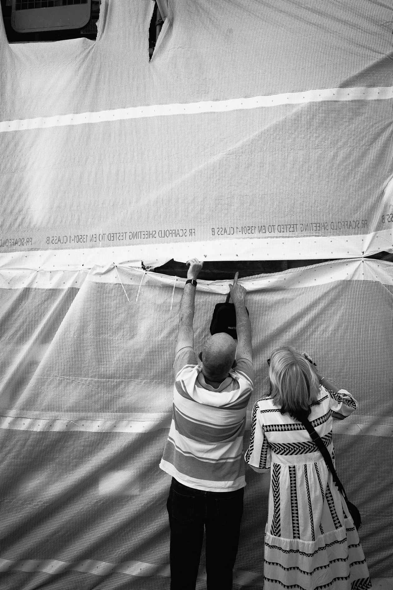 Two men and a woman inspecting and pointing at a large fabric or tarp, possibly at an outdoor event or construction site