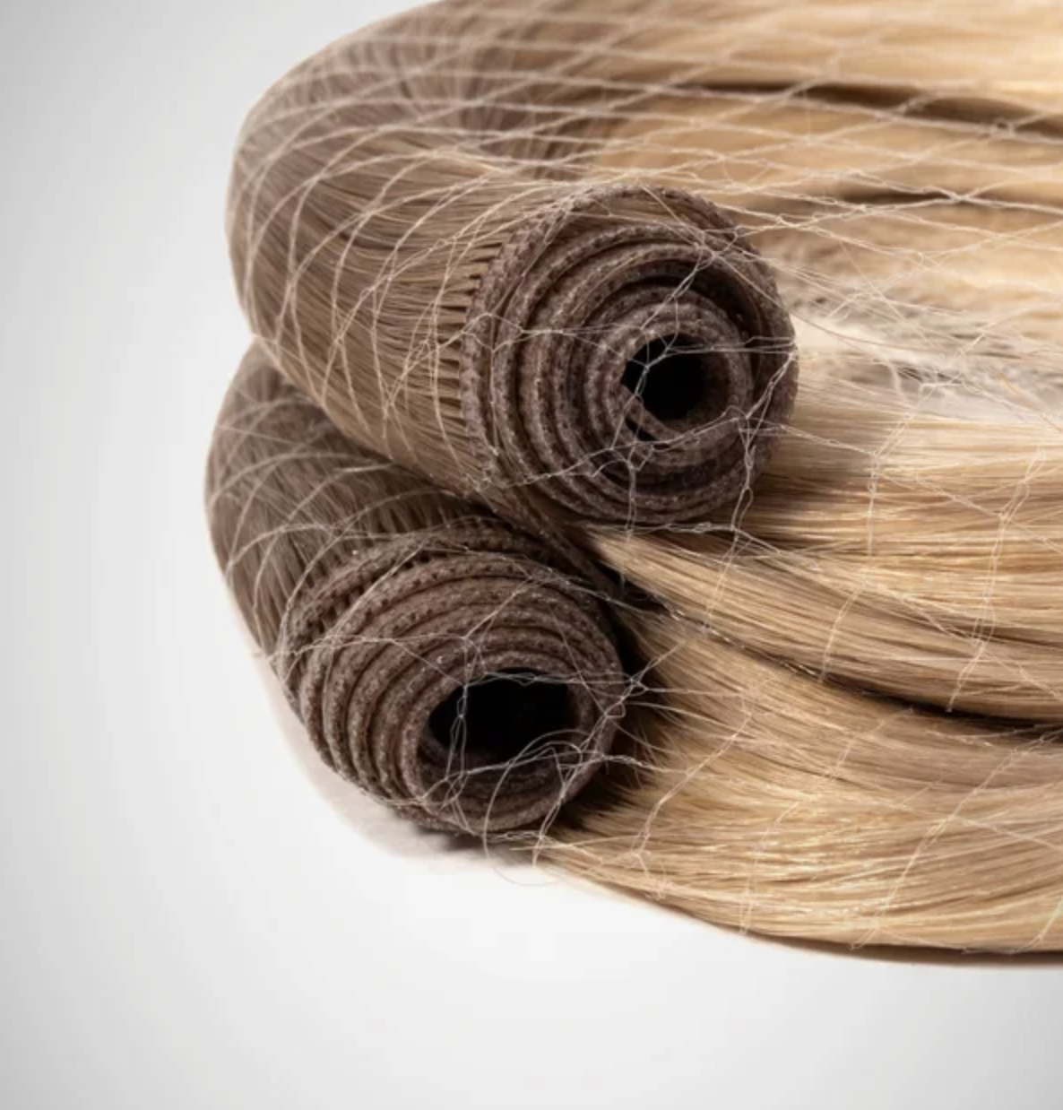 Close-up of blonde hair extensions with a rolled, brown, fabric cap at the base.