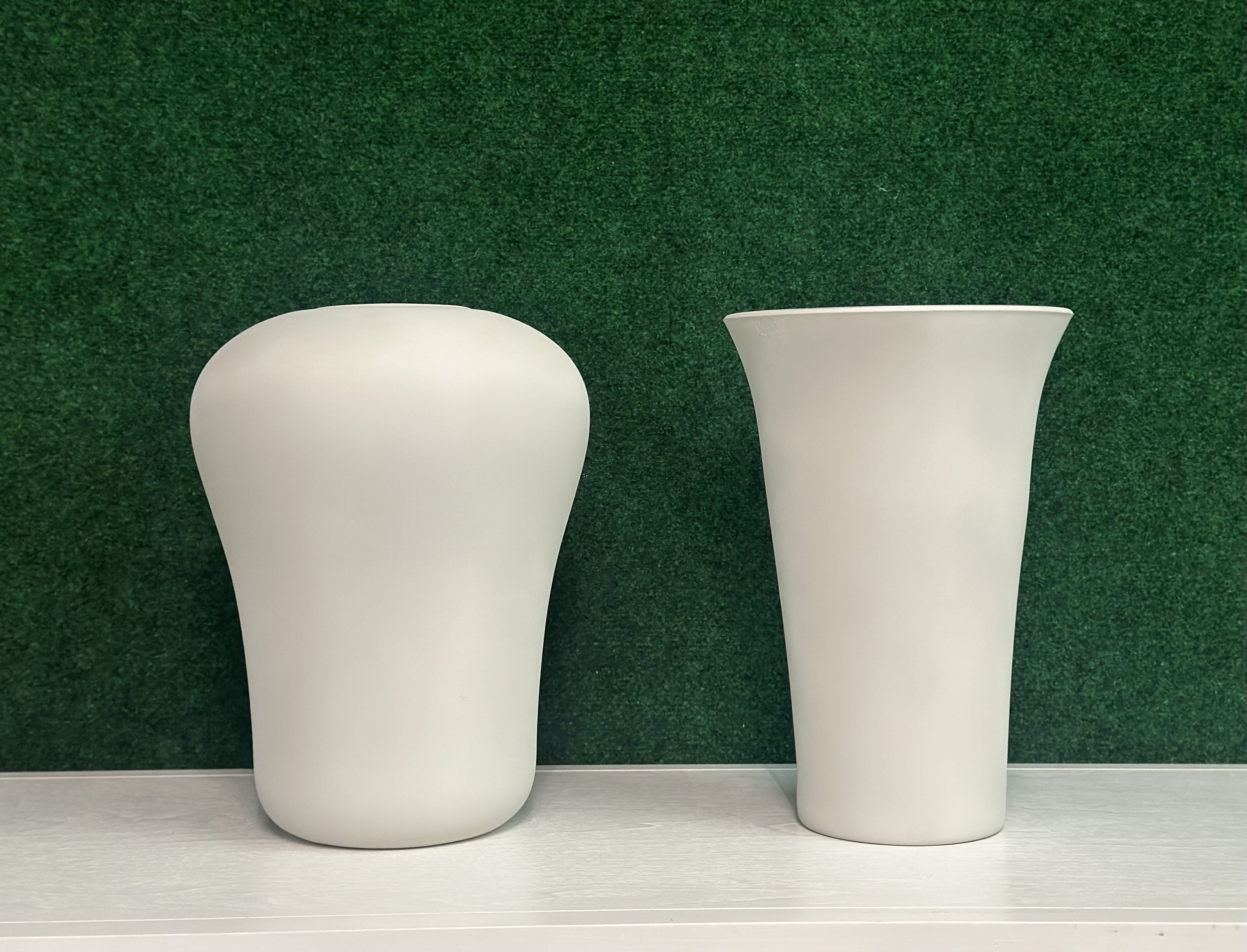Two white ceramic vases on a white surface with a green background.