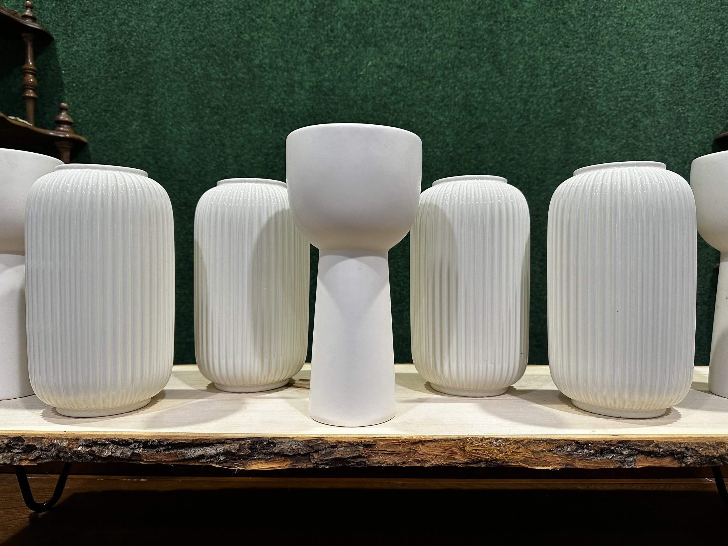 White ceramic vases with vertical ridges and a round bowl-shaped vase displayed on a wooden shelf against a green background.