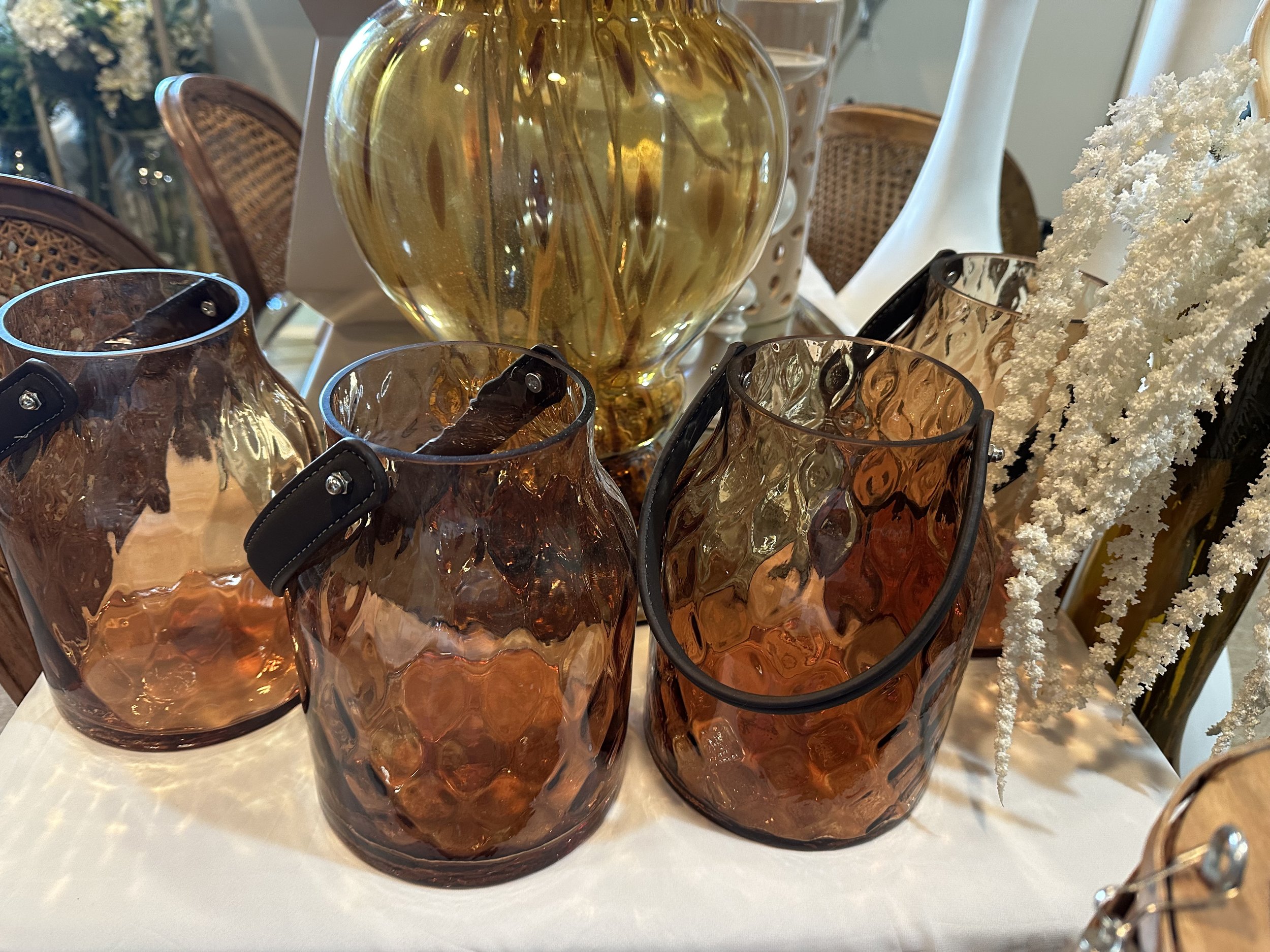 Amber glass vases with leather handles and a gold vase on a table, surrounded by decorative elements.