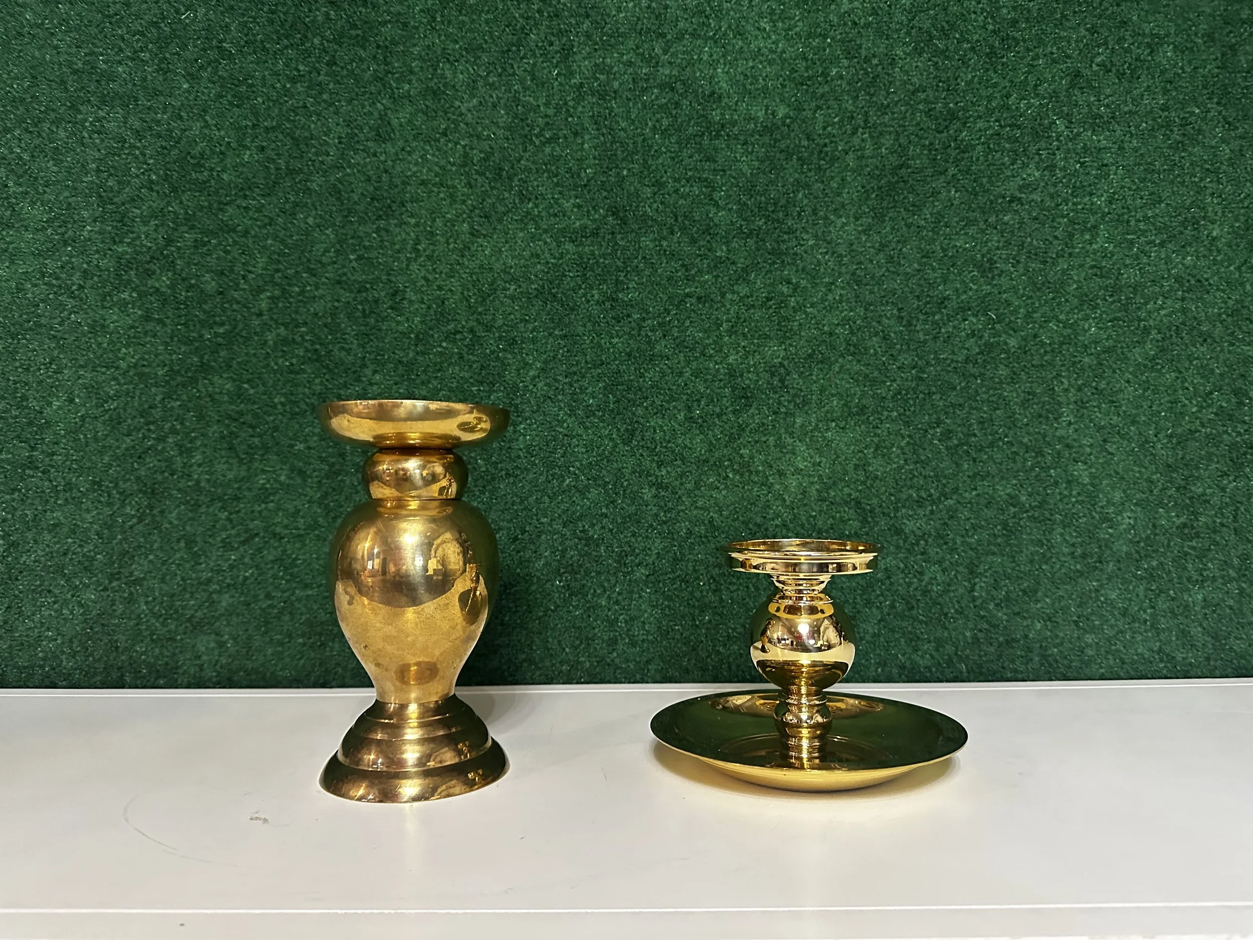 Two brass candlestick holders on a white surface with a green background.