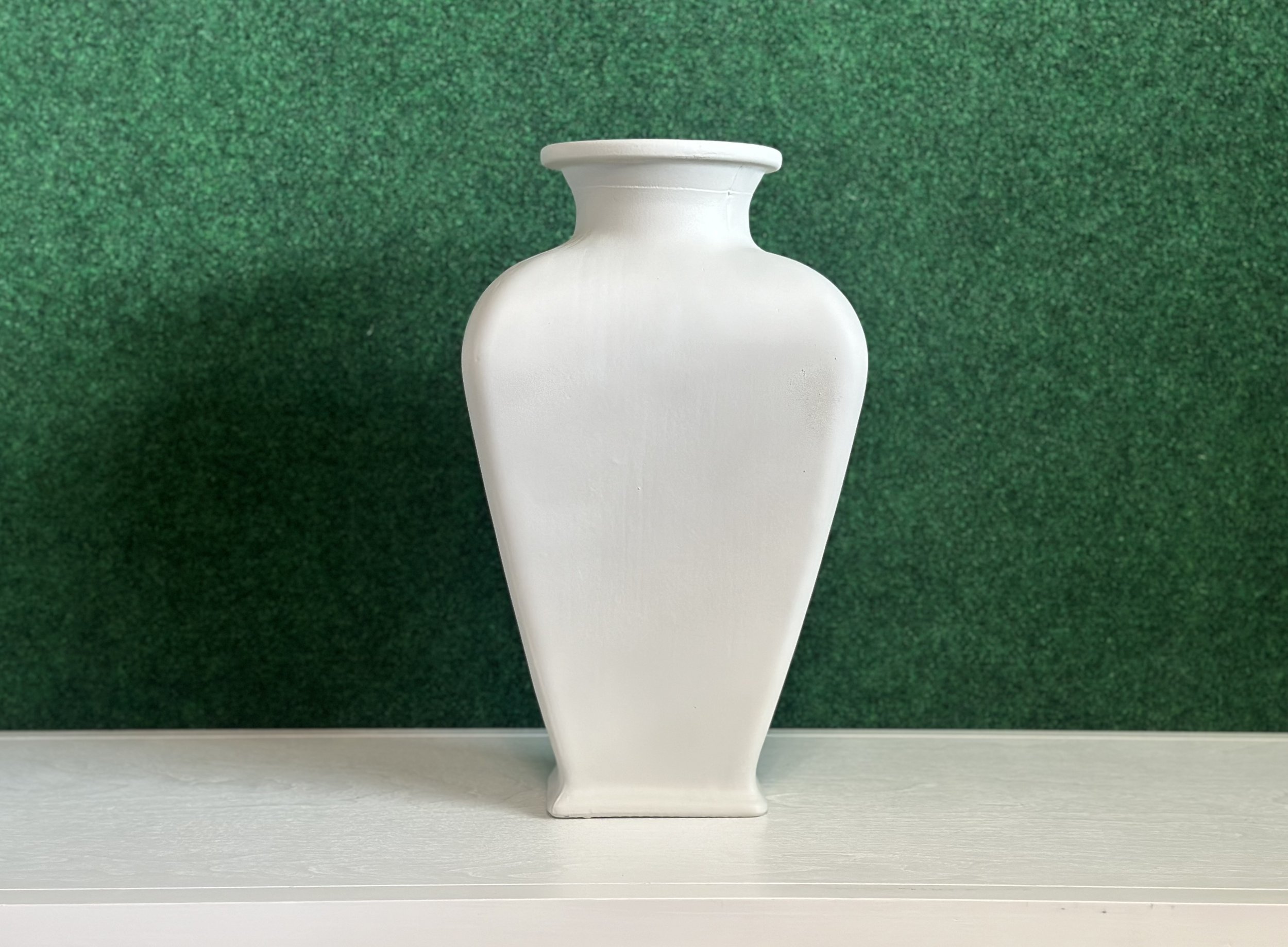 A white vase on a shelf against a green background.