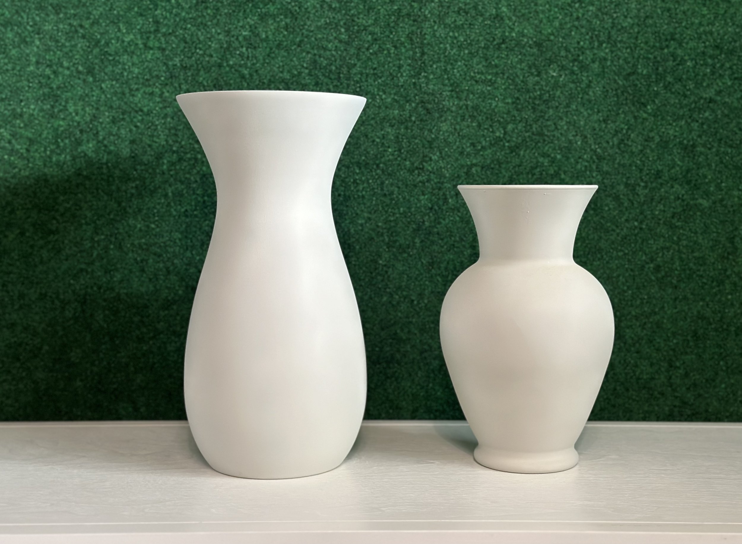 Two white ceramic vases of different sizes against a green textured background.