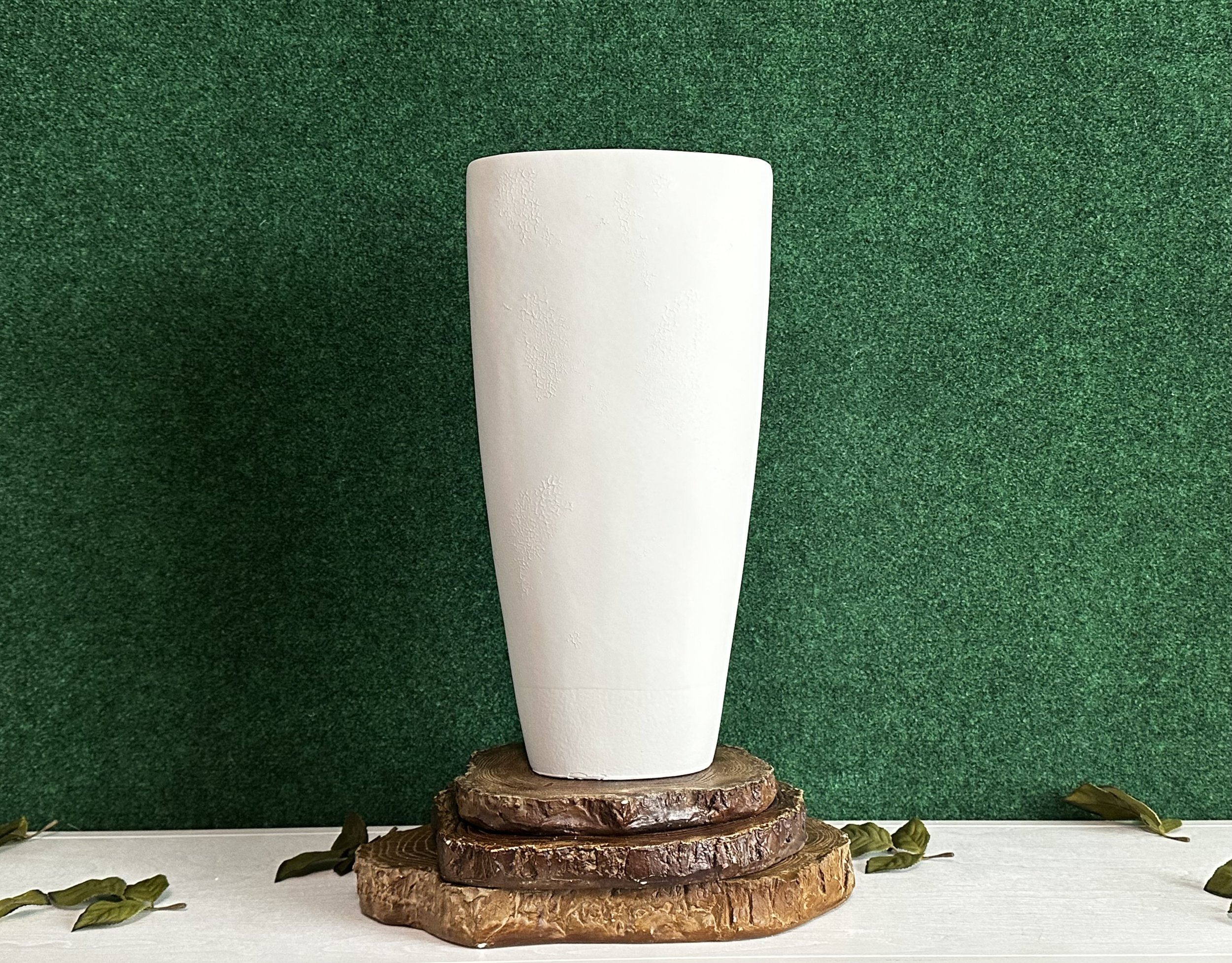 Tall white vase on wooden base with green background